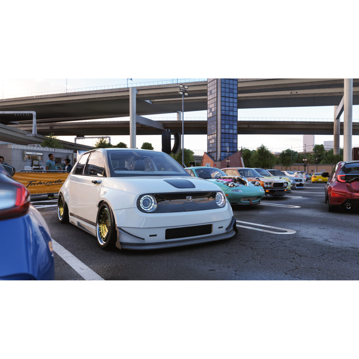 Una Honda E bianca è parcheggiata, con una fila di auto colorate accanto sotto un cavalcavia.