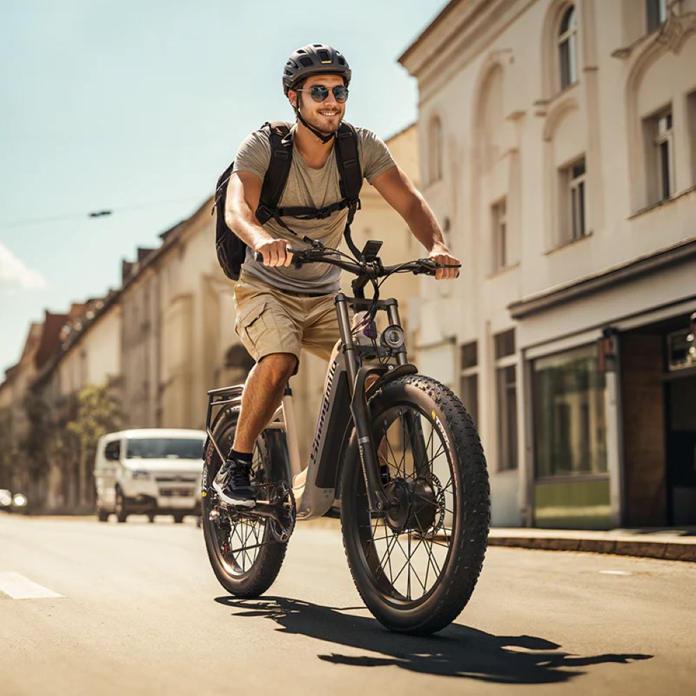 Uomo in e-bike in città con edifici e furgone bianco.