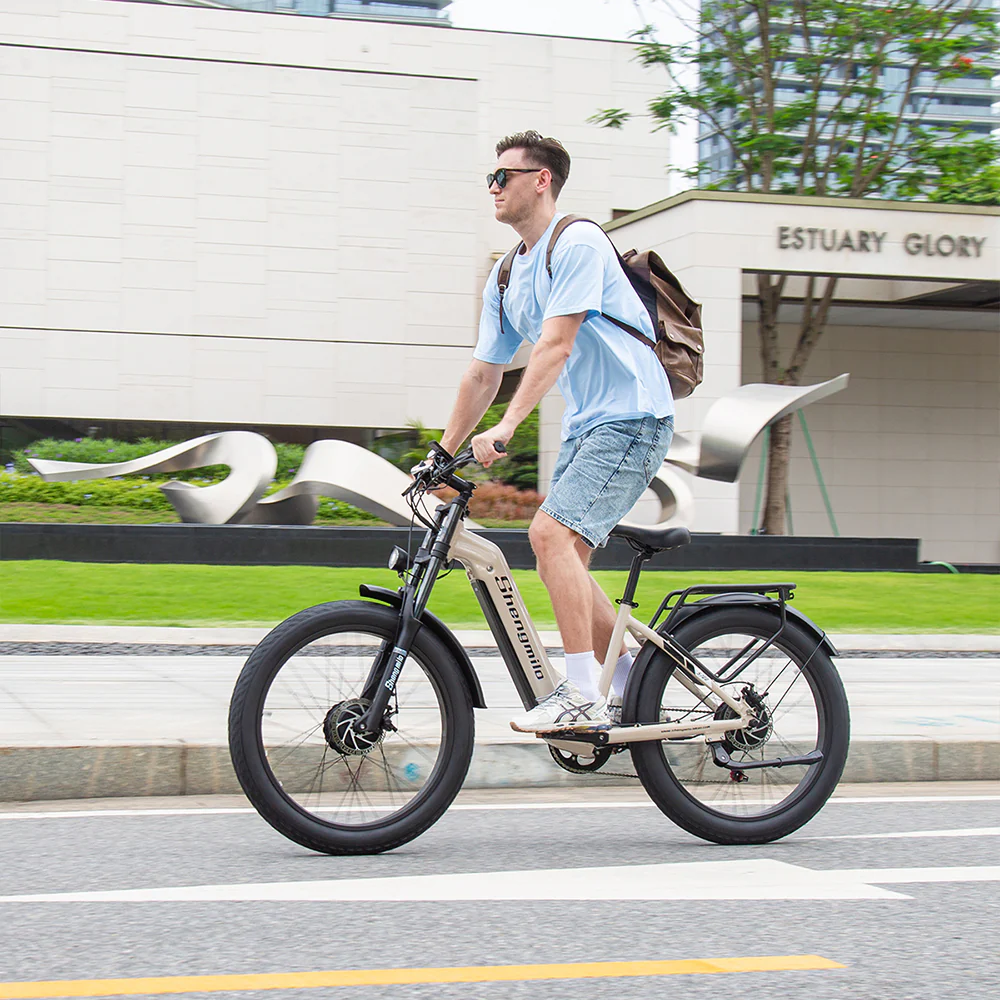 Un uomo guida una e-bike beige in strada con edifici sullo sfondo.