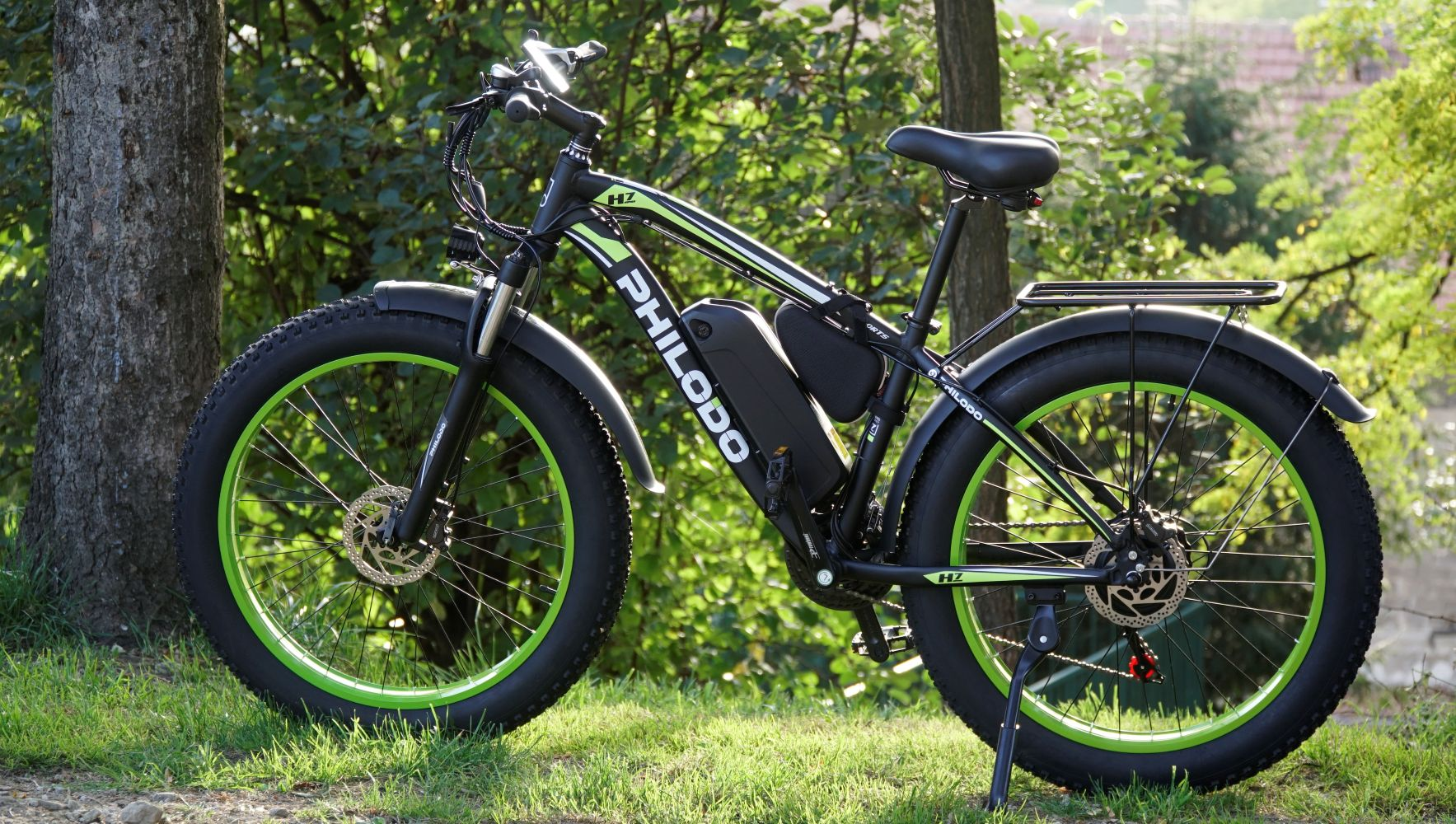 Una e-bike nera con copertoni larghi e cerchi verdi è sull'erba.