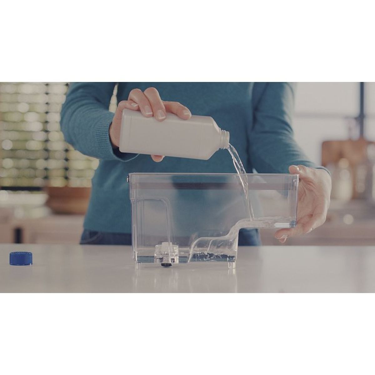 Eine Person gießt Flüssigkeit aus einer weißen Flasche in einen durchsichtigen Behälter.