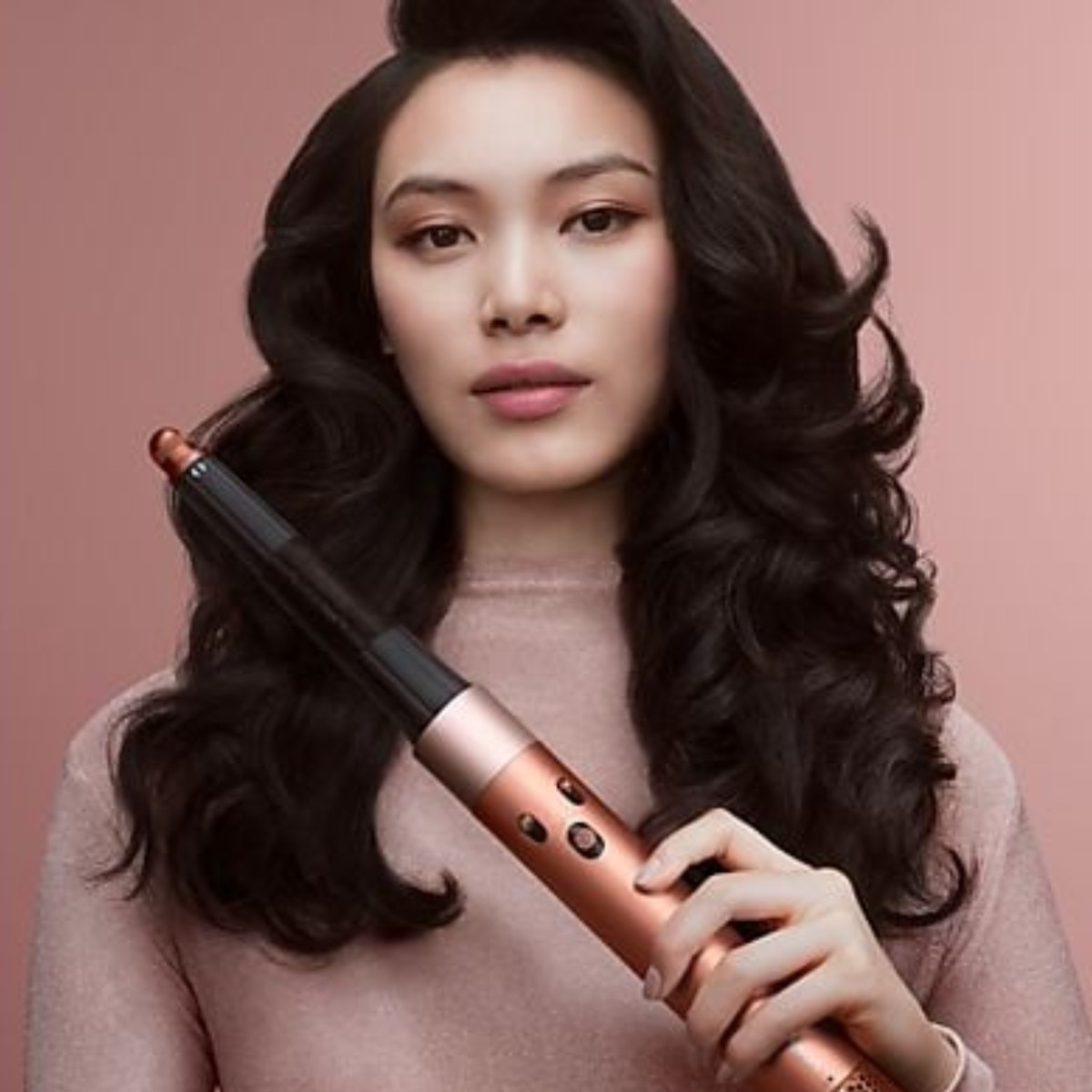 Frau mit langen dunklen Haaren hält ein roségoldenes Haarstyling-Gerät.