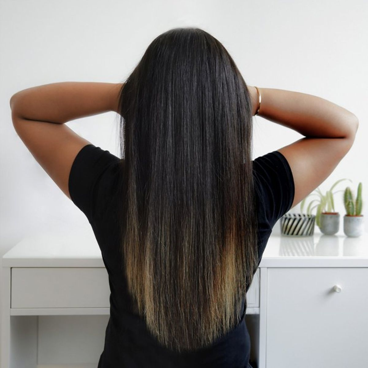 Vista posteriore di una donna con capelli lunghi, lisci e castano scuro e braccialetto d'oro.