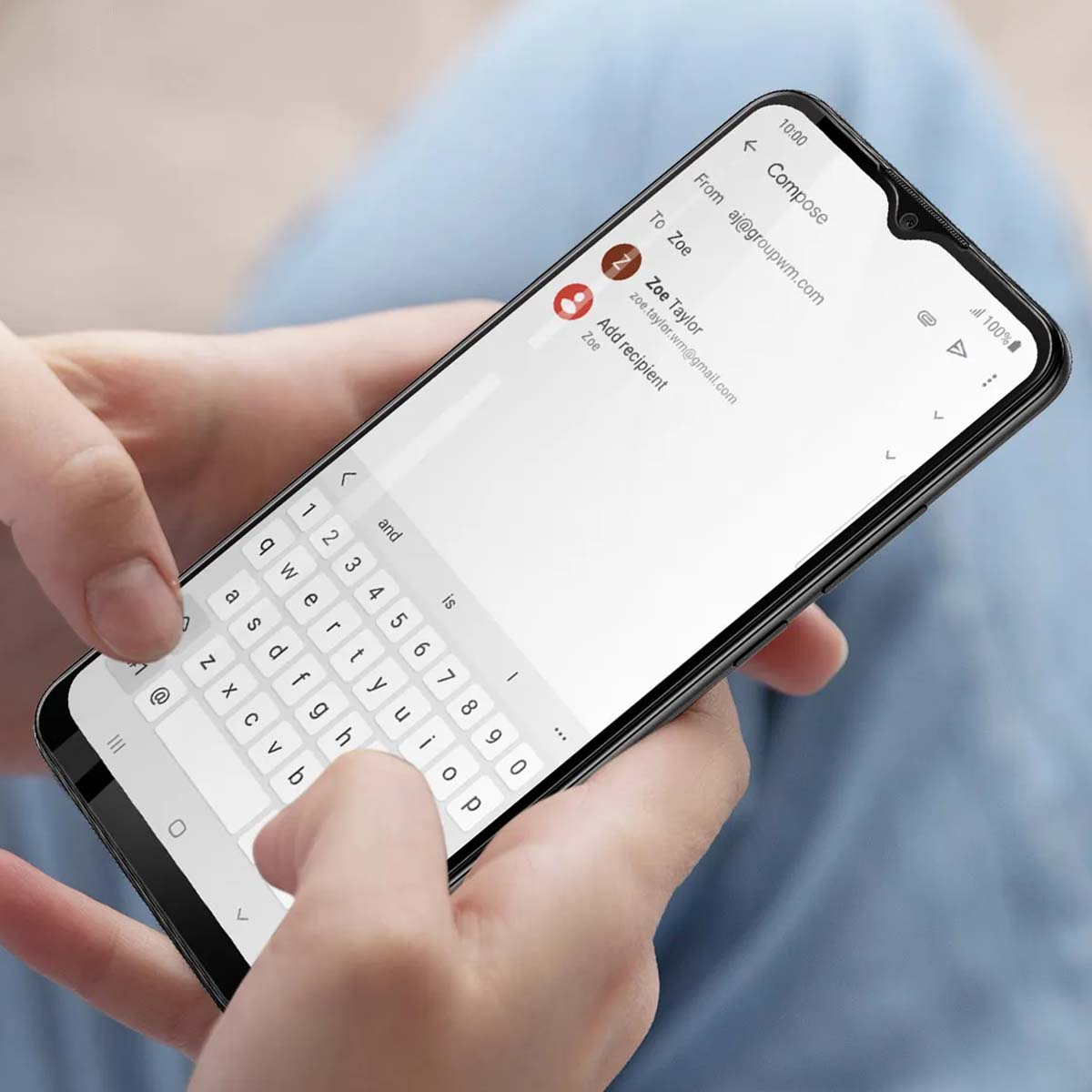 Mains tenant un smartphone affichant un écran de composition d'e-mail avec clavier.