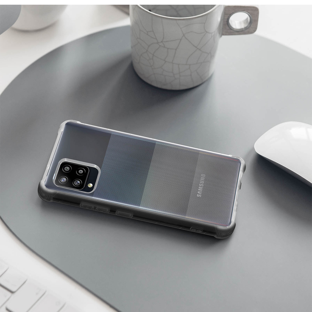 Uno smartphone con quattro fotocamere poggia su un tappetino grigio accanto a un mouse e una tazza.