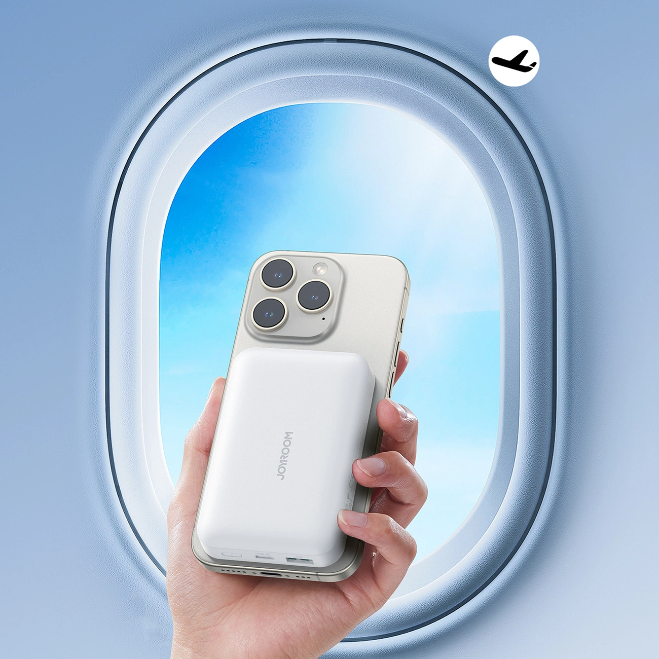 Eine Hand hält ein Smartphone mit angebrachtem weißem Akku vor einem Flugzeugfenster.