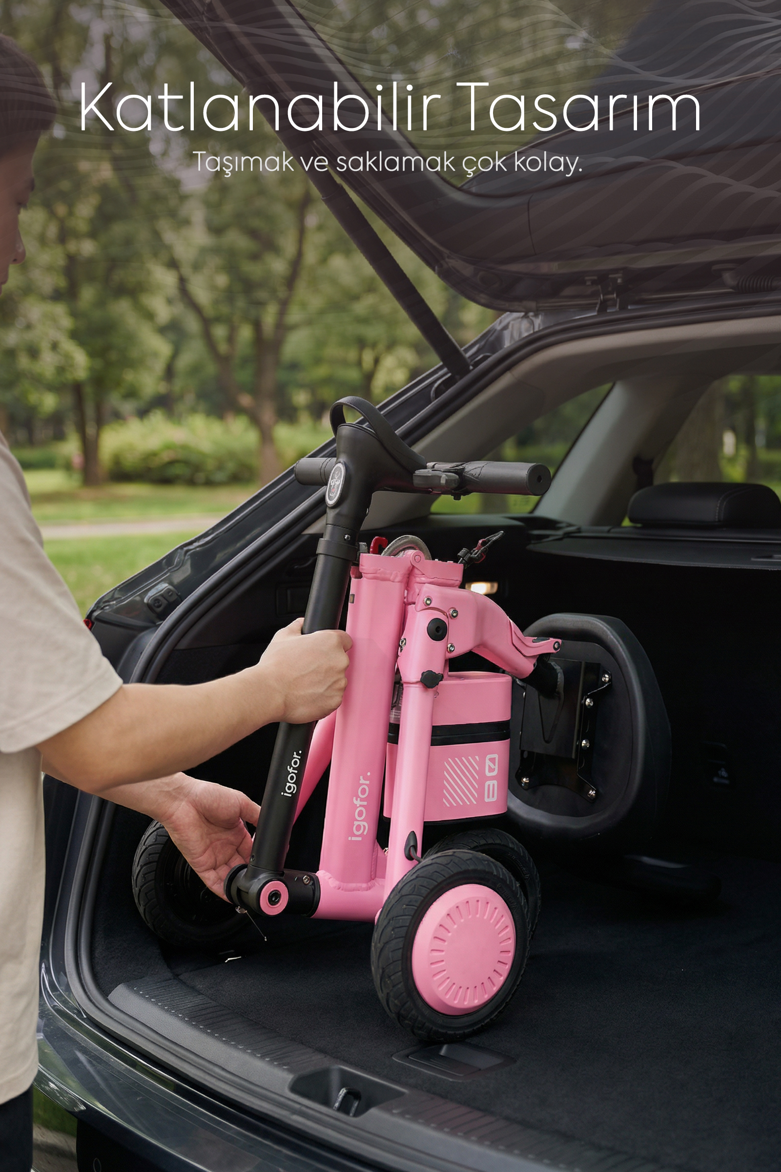 Bir kişi, katlanabilir pembe bir scooter'ı açık araba bagajına yüklüyor.