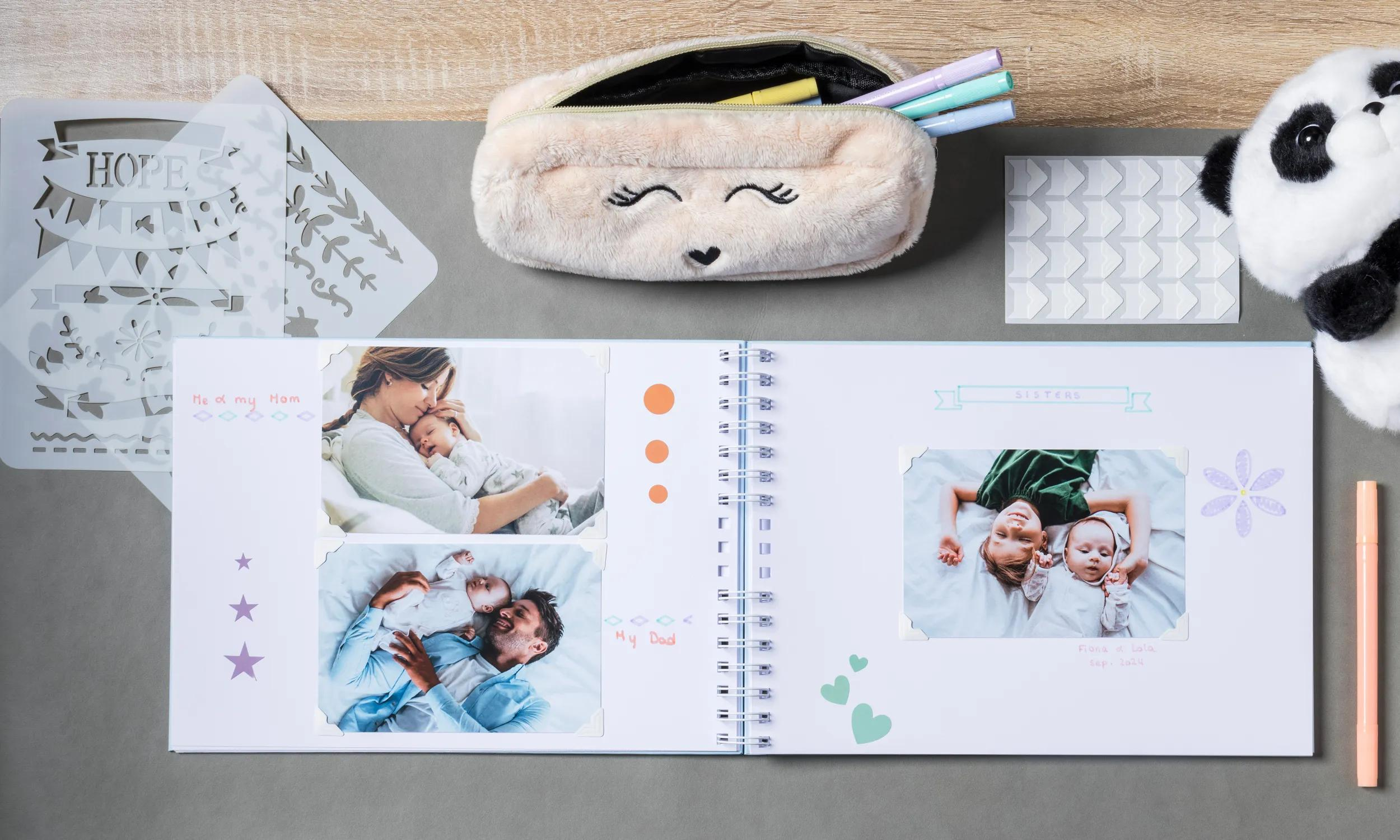 Un álbum de recortes abierto con fotos de bebés, plantillas, bolígrafos y un peluche de panda.