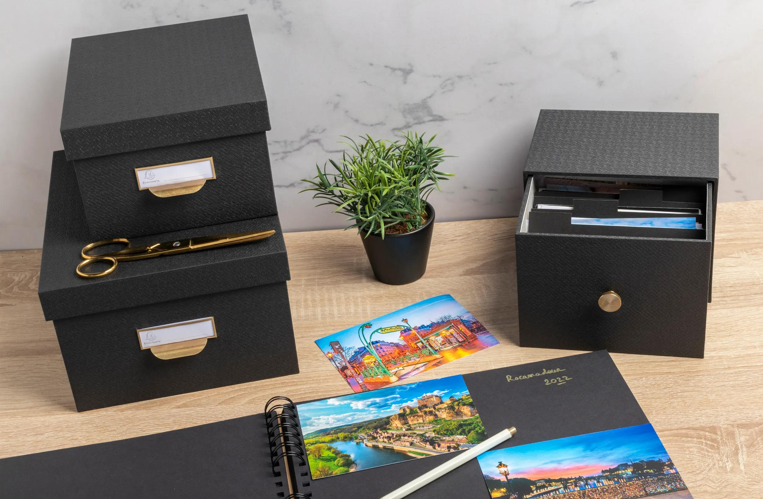 Cajas de almacenamiento negras, tijeras, planta, postales y un cuaderno.