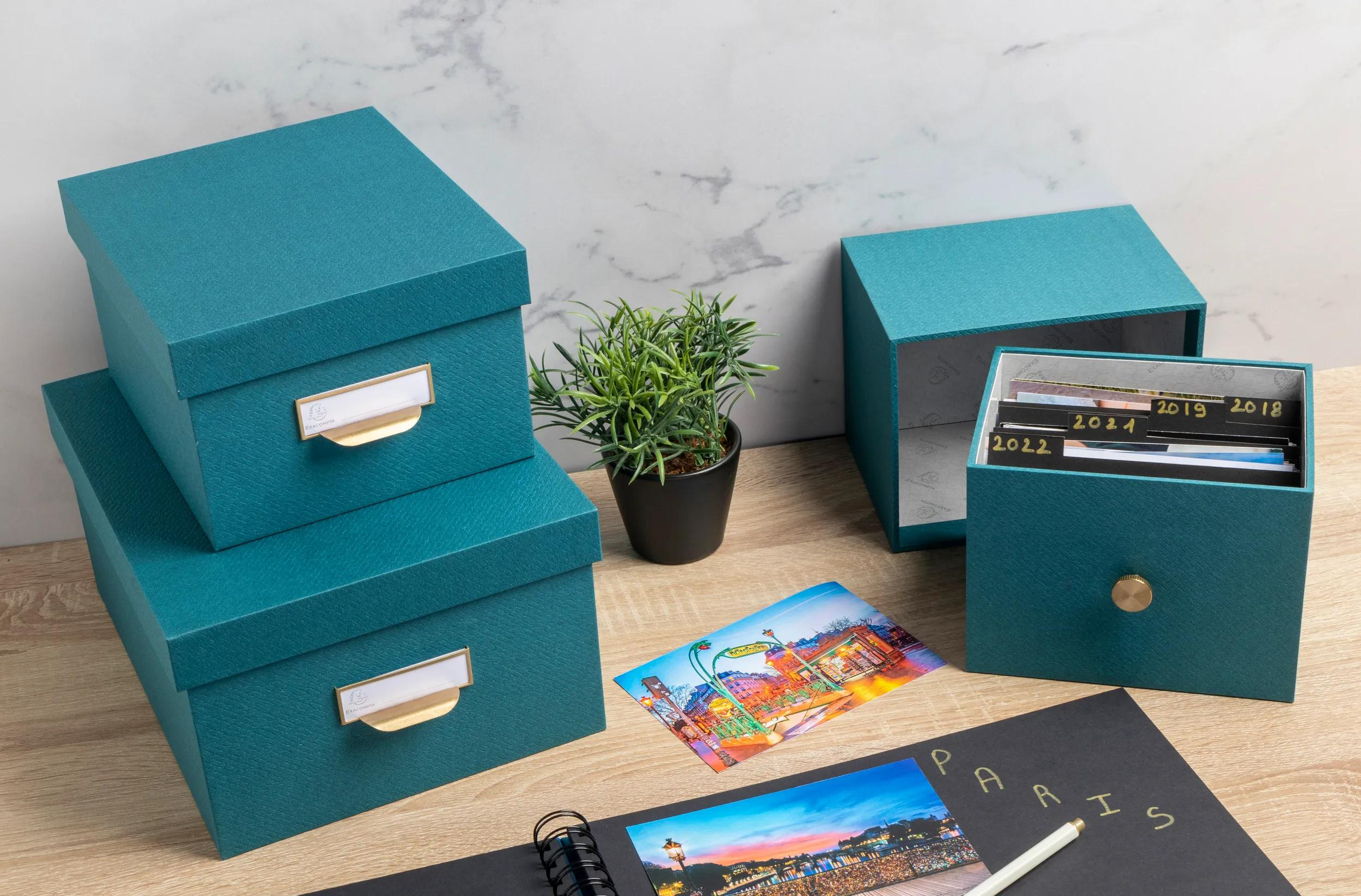 Cajas de almacenamiento turquesas con fotos, planta y cuaderno en mesa madera.