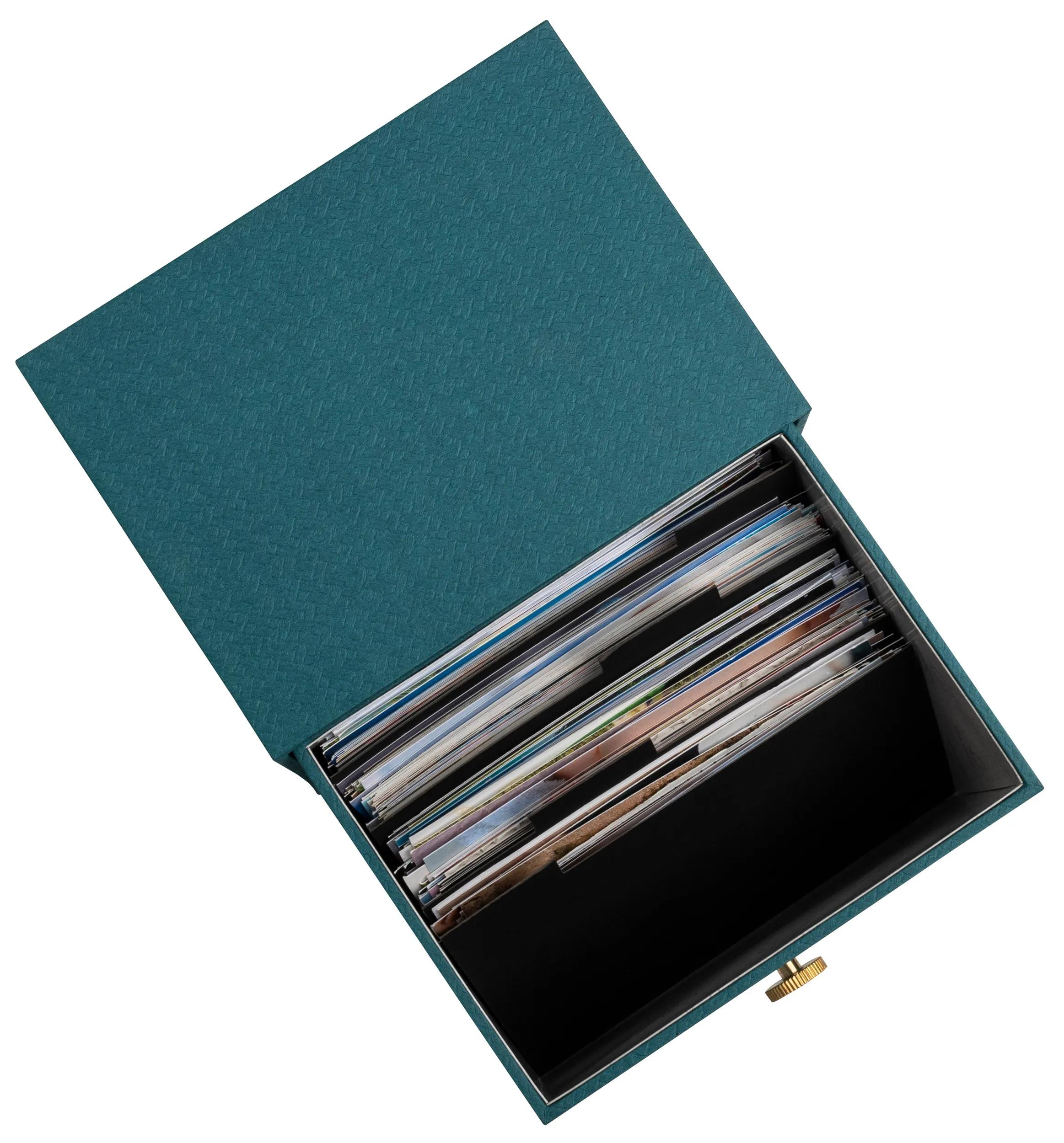 Una caja azul verdosa abierta llena de fotos, con un pequeño pomo dorado en el lateral.