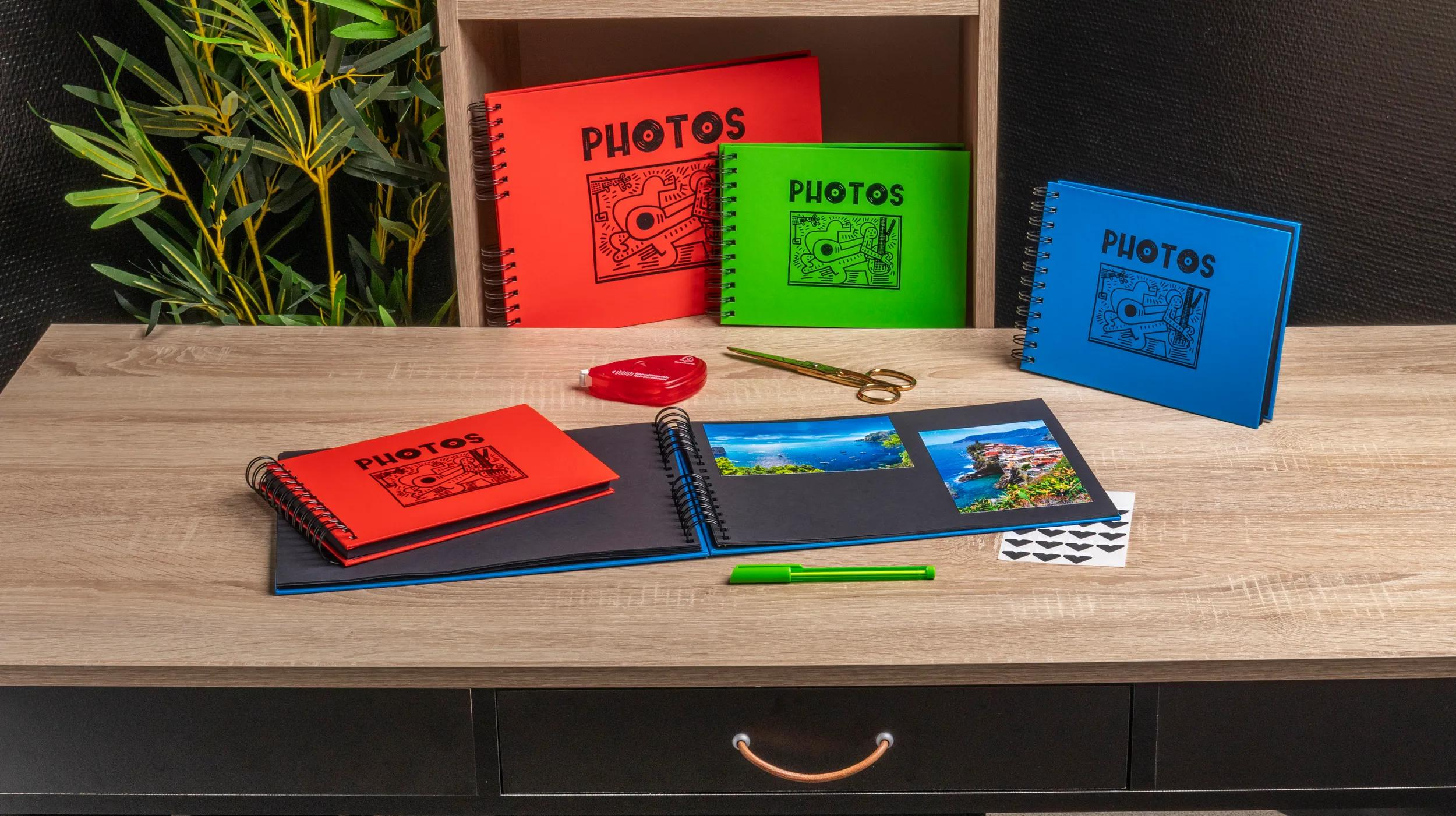 Álbumes de fotos rojos, verdes y azules sobre un escritorio de madera con fotos y suministros.