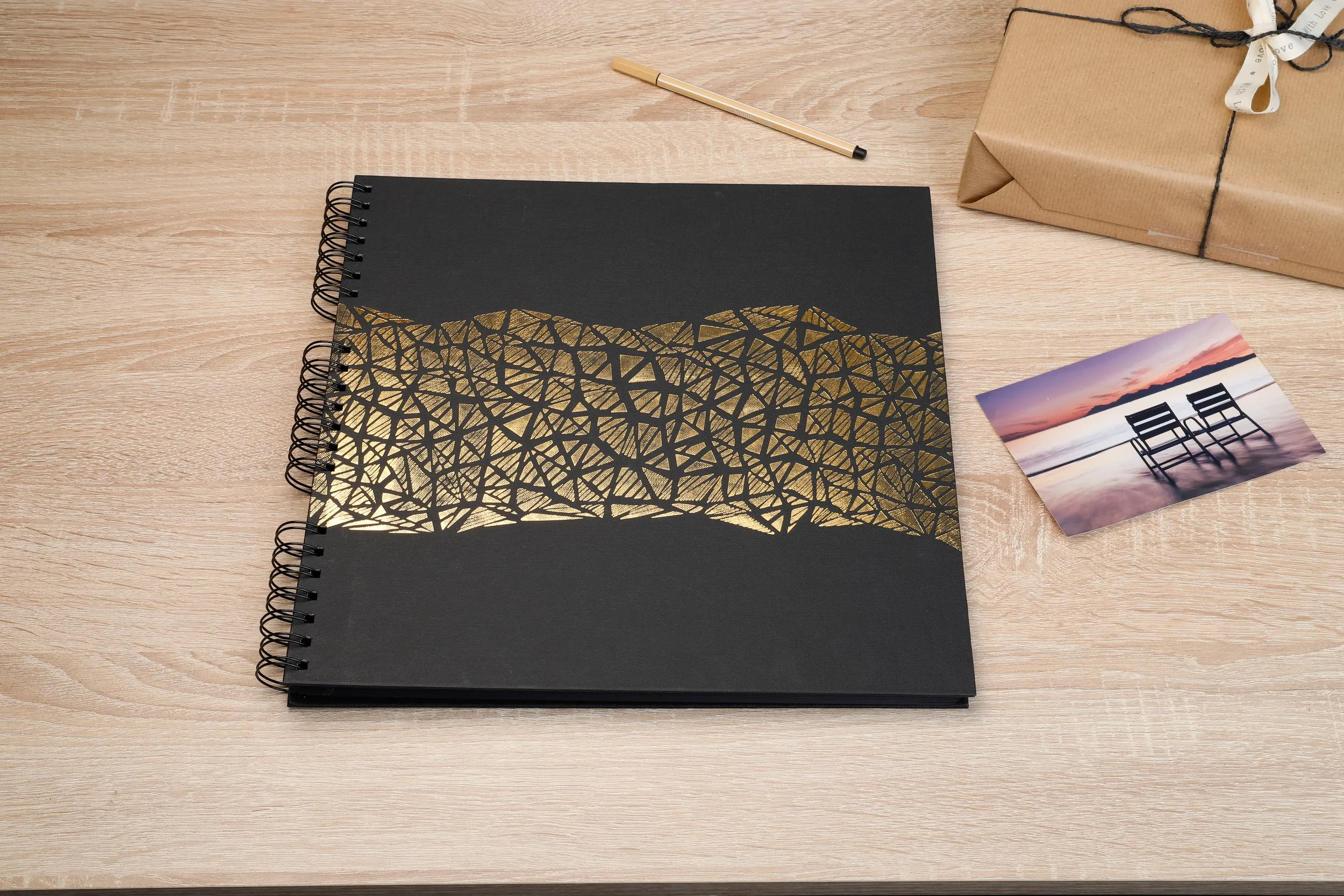 Un cuaderno negro con patrón dorado, bolígrafo, regalo y foto en mesa de madera.