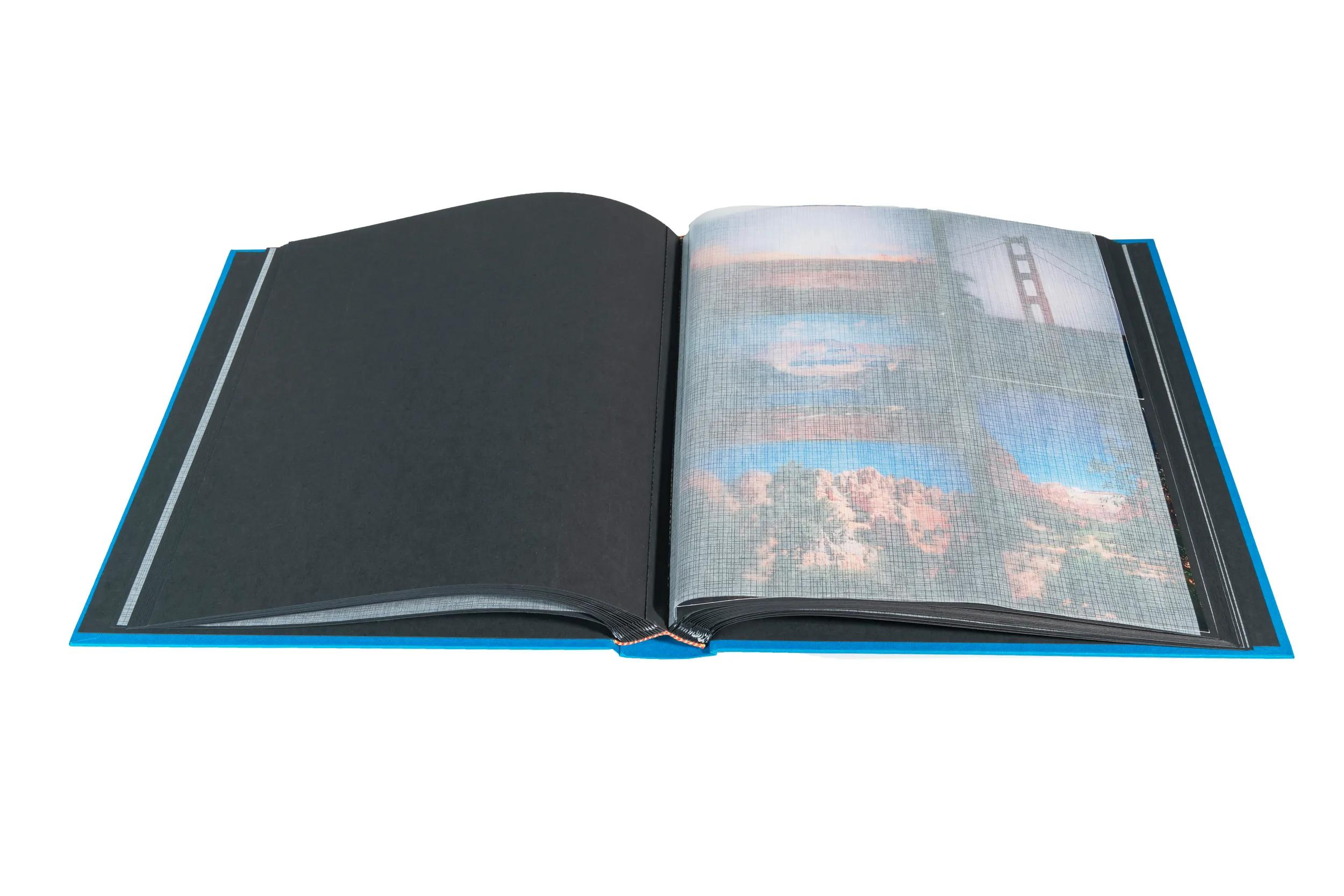 Un álbum de fotos azul abierto con páginas negras que muestran fotos de puentes y paisajes.