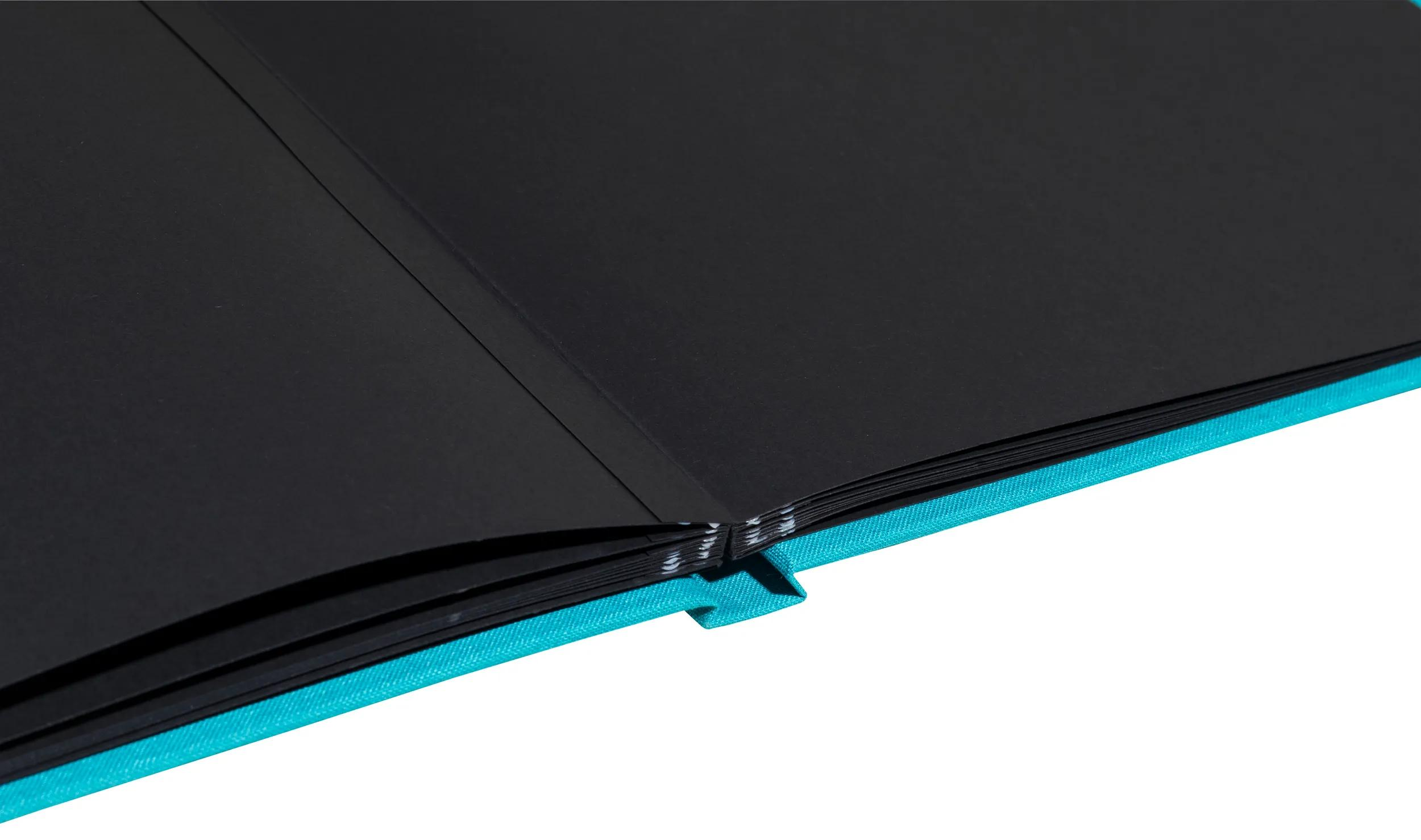 Un cuaderno abierto con cubierta turquesa y páginas negras.