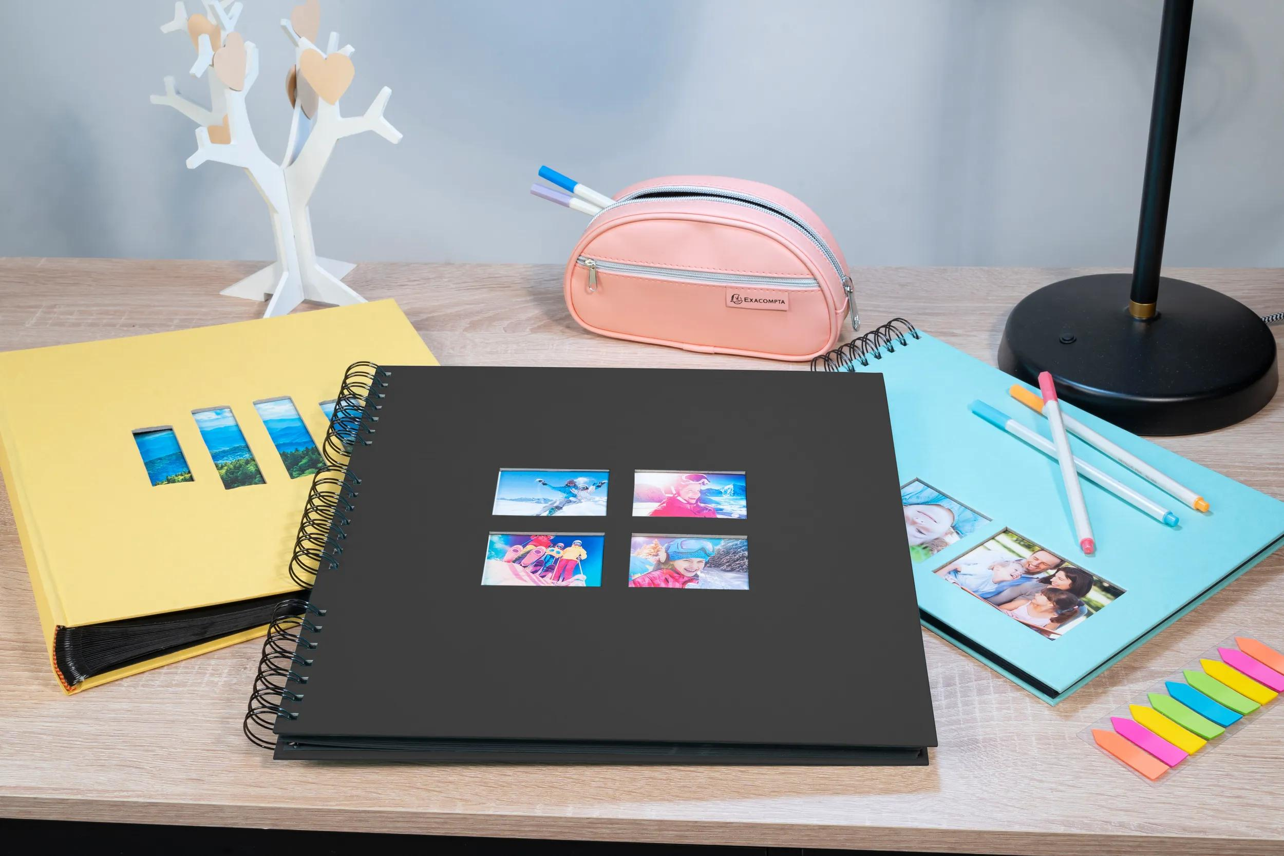 Un escritorio con álbumes de fotos, bolígrafos, una lámpara y decoración de árbol.