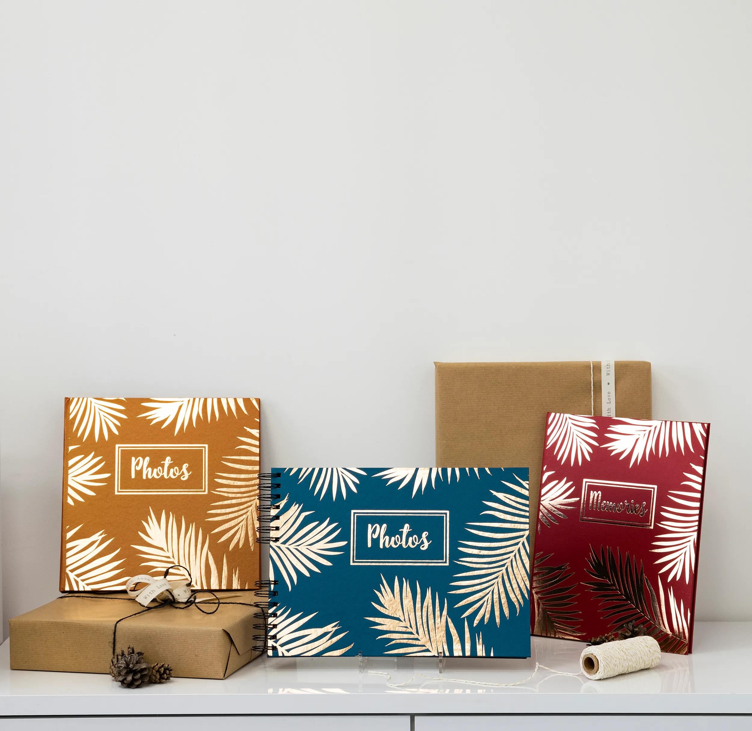 Tres álbumes de fotos con estampado de hojas en un estante junto a regalos.