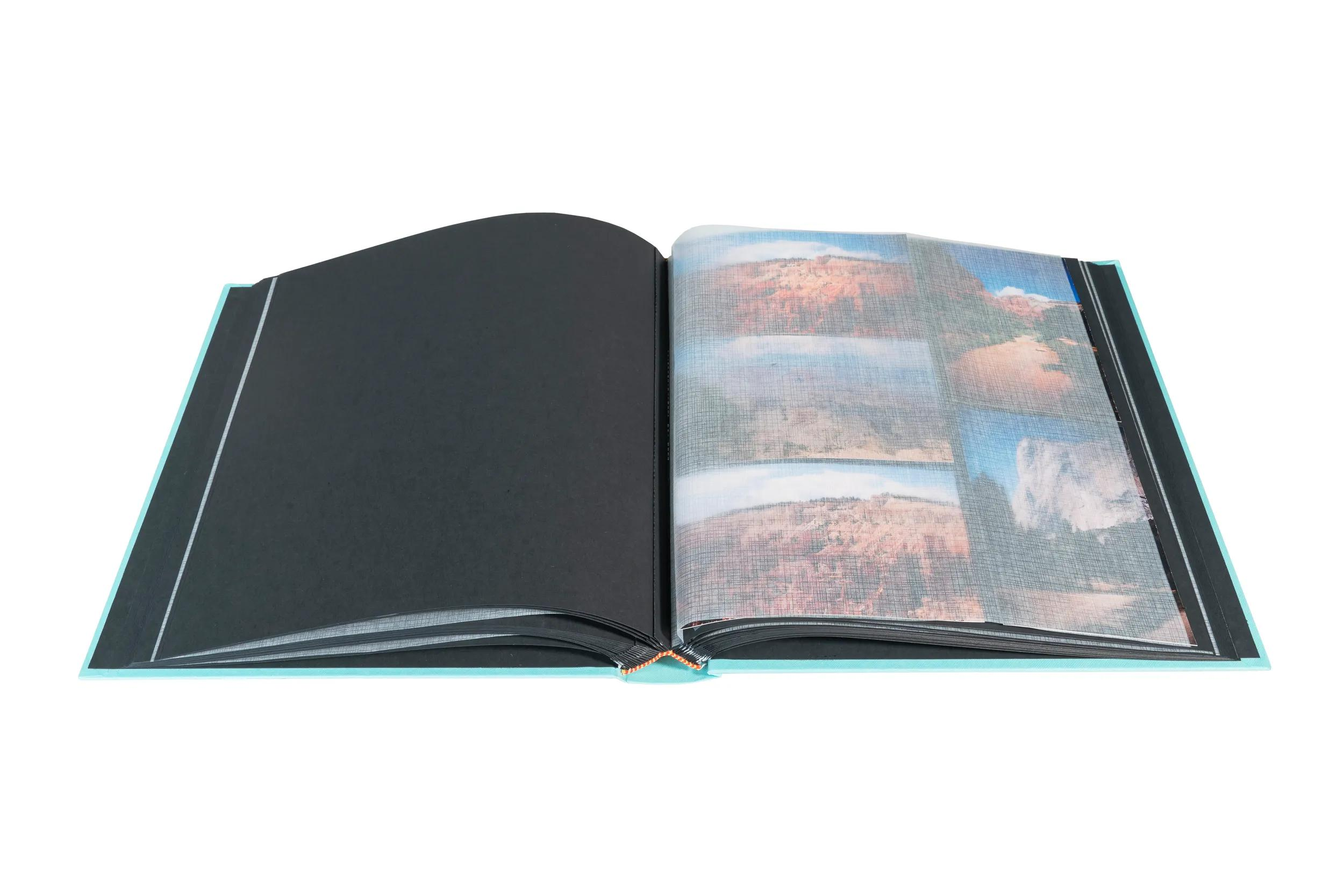 Un álbum de fotos azul claro abierto muestra páginas negras y fotos de paisajes.
