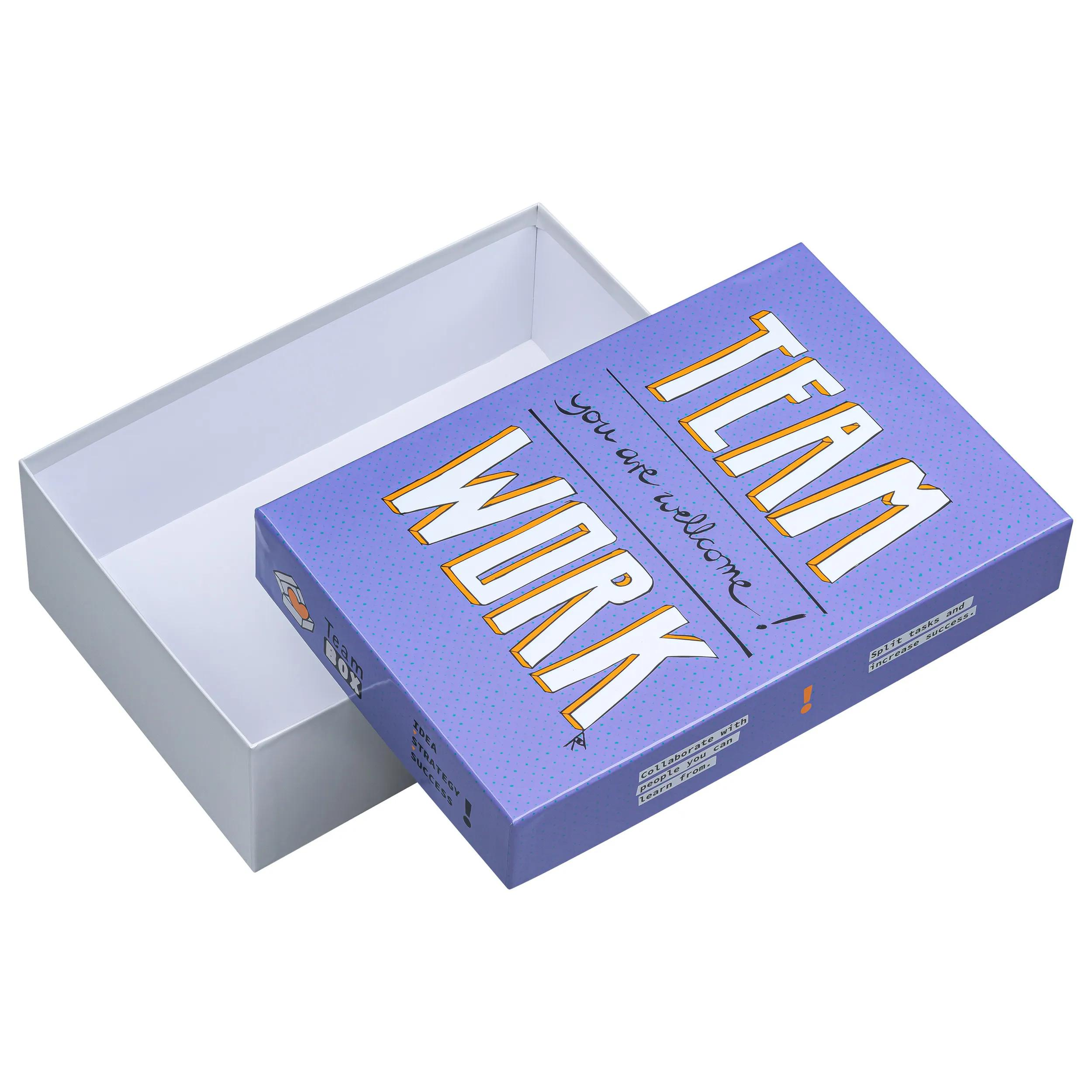 Caja abierta con tapa. Tapa morada con texto "TEAM WORK".