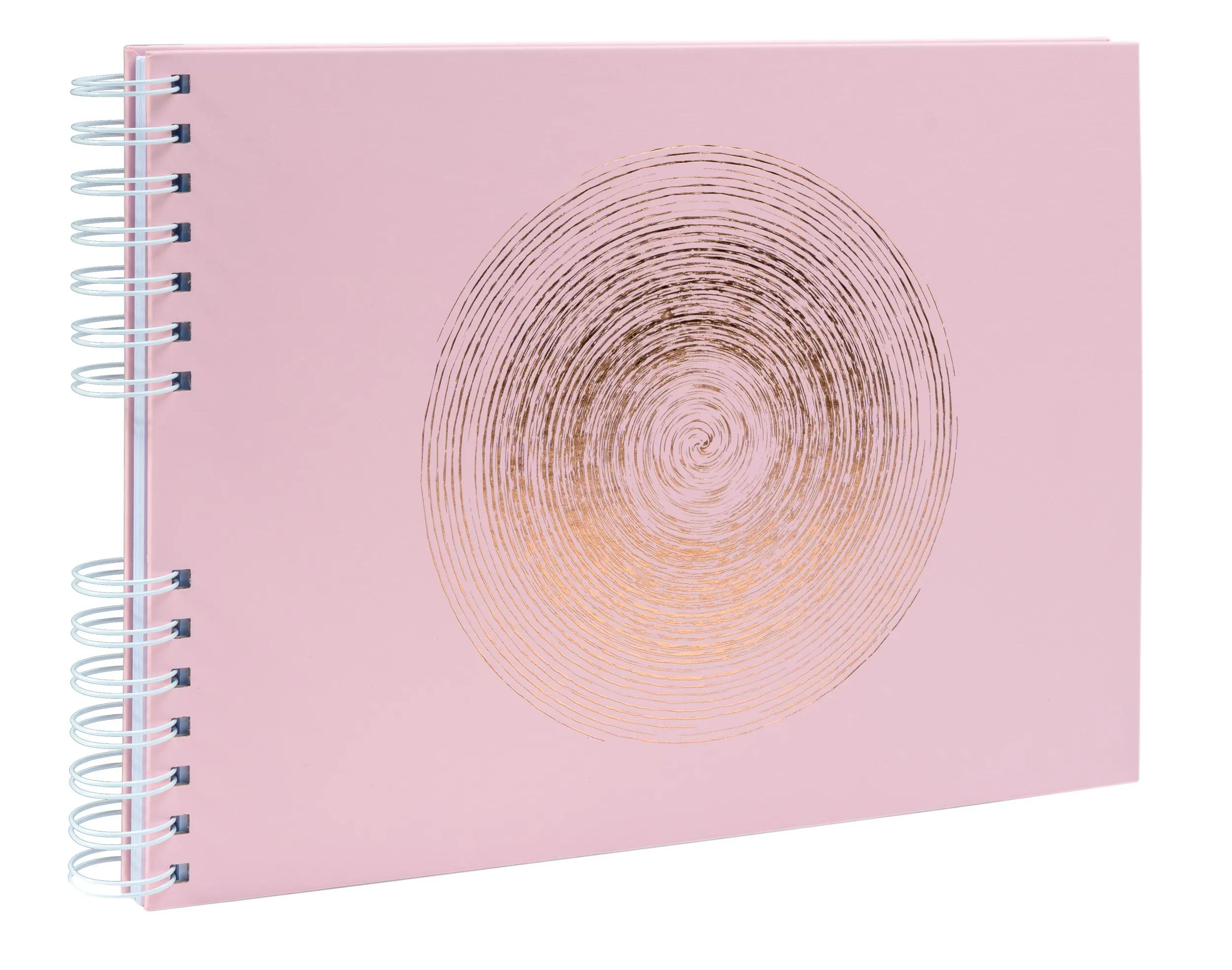 Un cuaderno espiral rosa con un patrón de círculo dorado y encuadernación en espiral blanca.