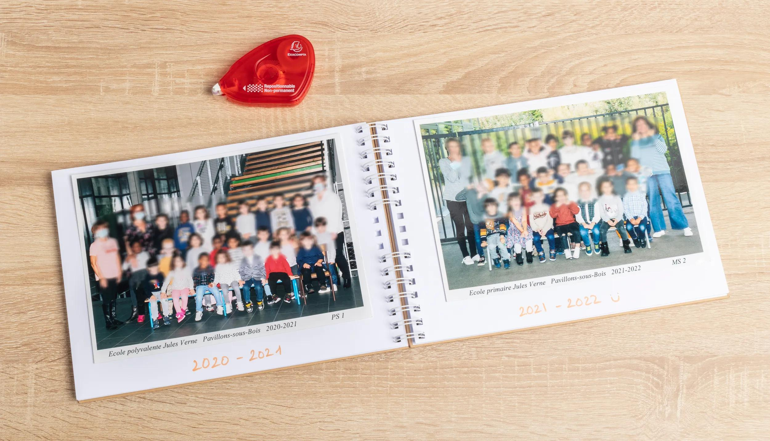 Un dispensador de cinta rojo junto a un álbum de fotos abierto con dos fotos de clase.