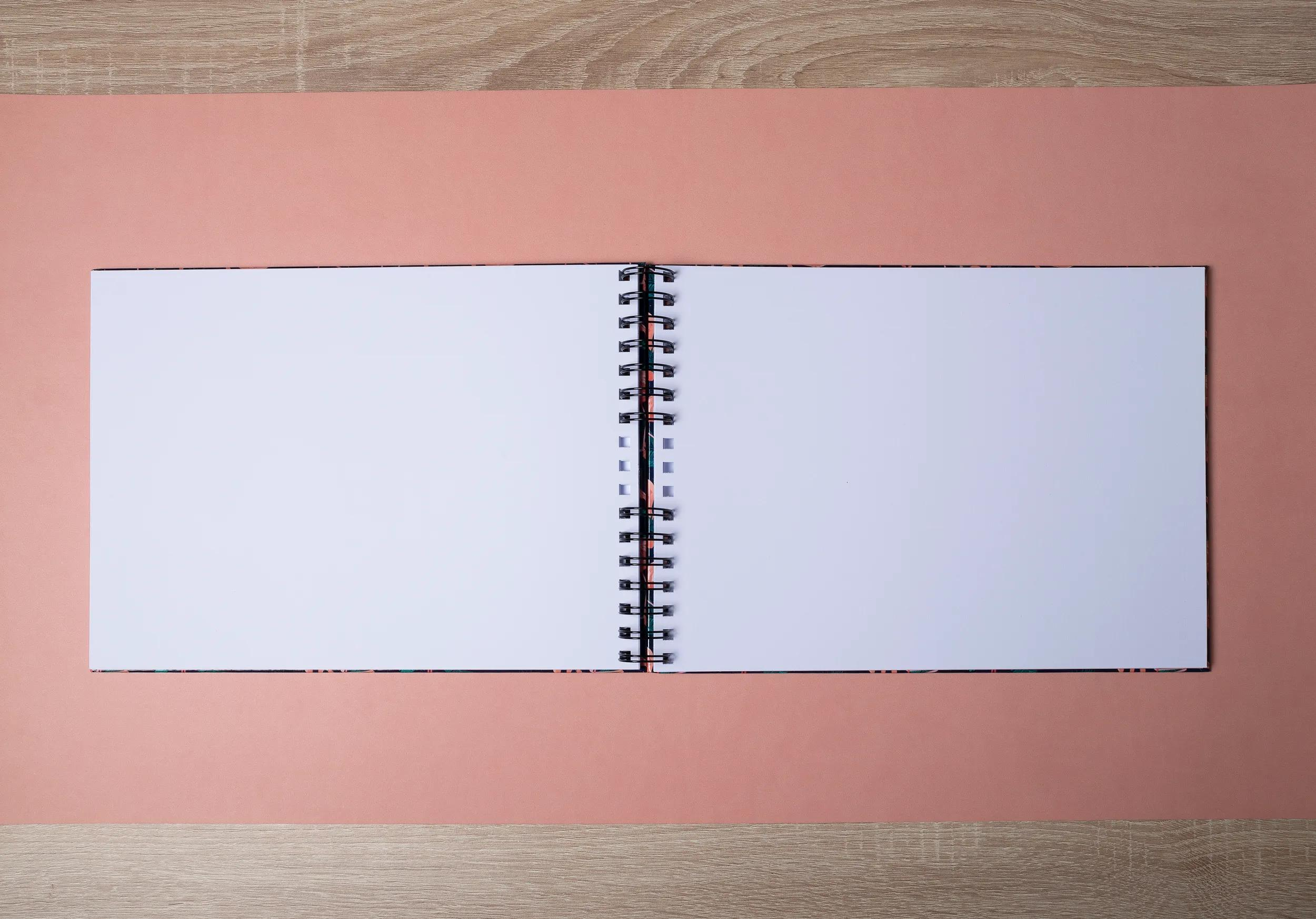 Un cuaderno abierto con páginas en blanco sobre fondo rosa y de madera.