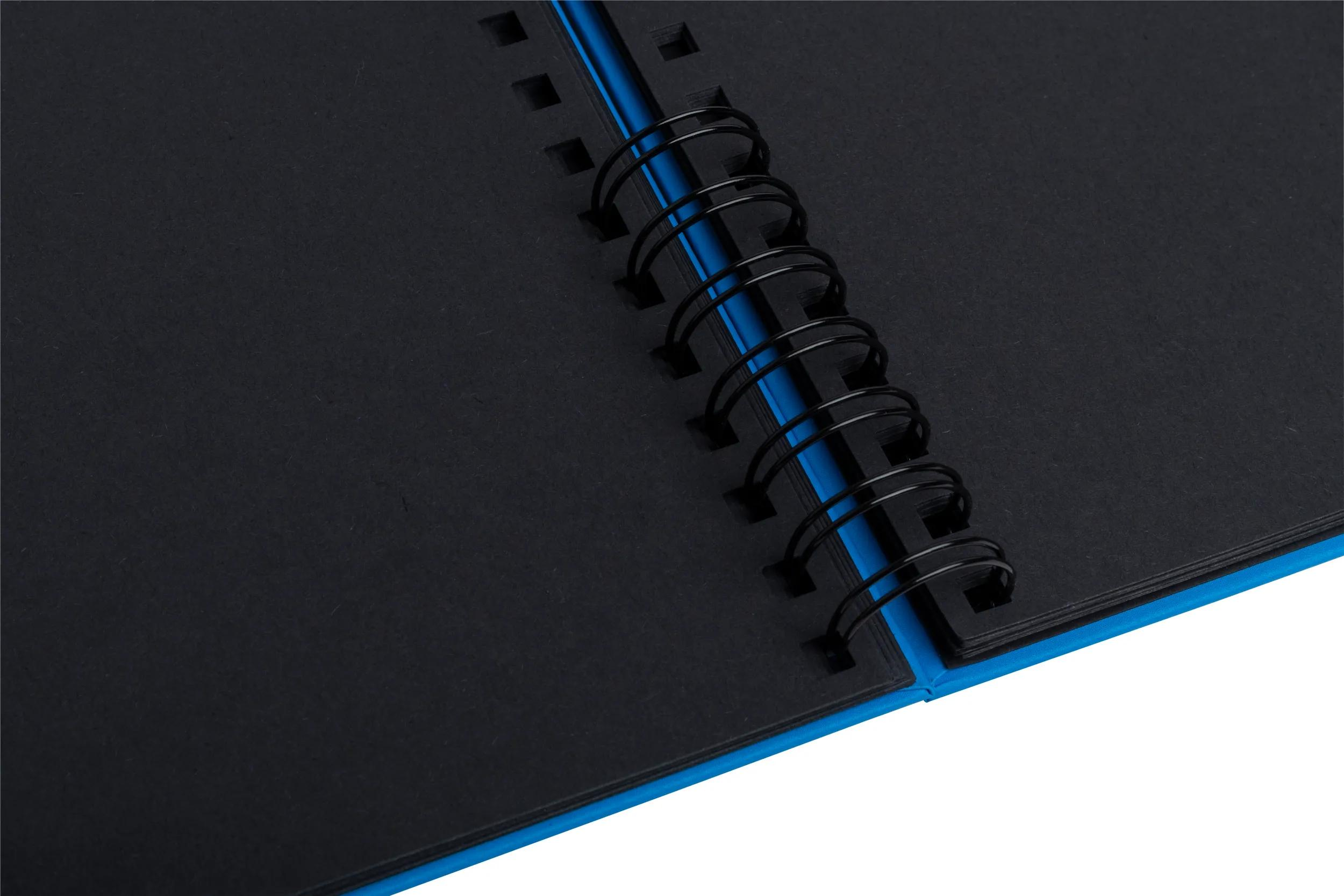 Un cuaderno abierto con páginas negras y encuadernación de espiral azul.