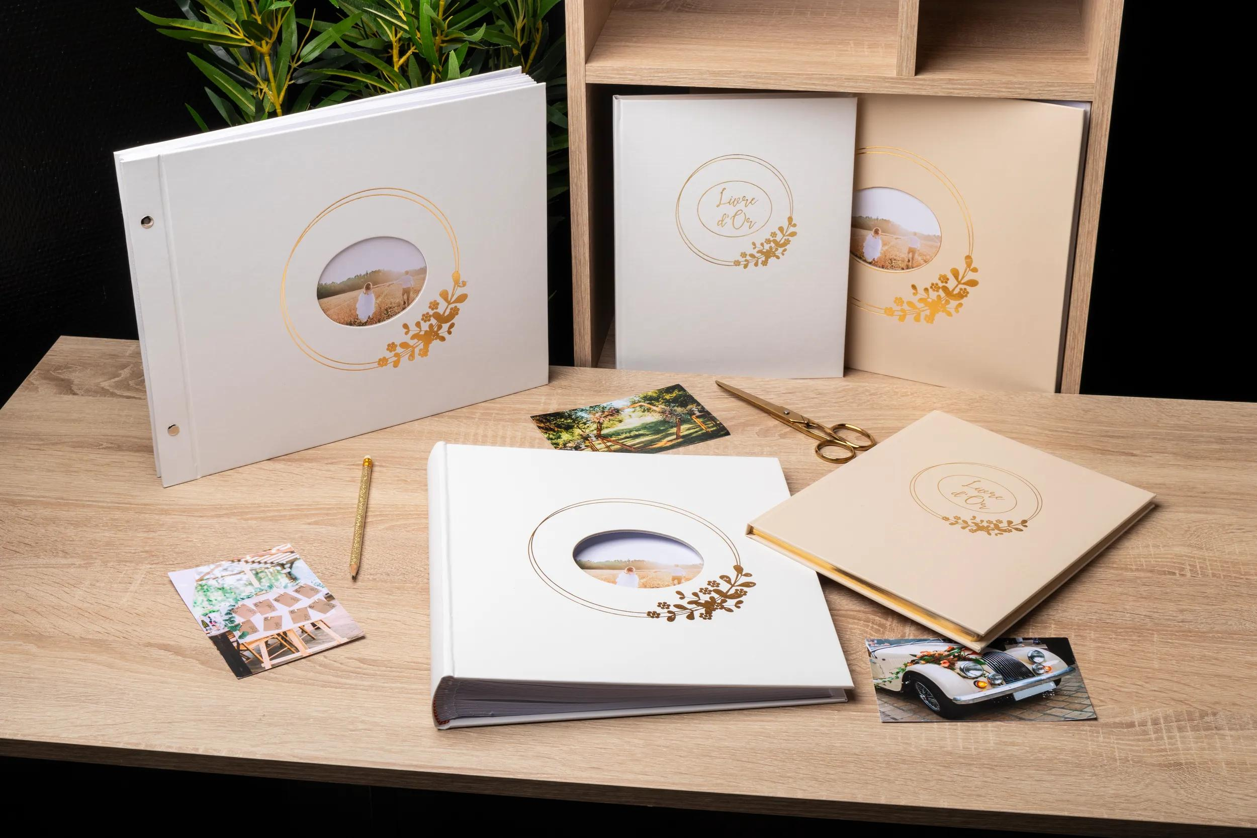 Álbumes de fotos blancos y crema con adornos dorados sobre una mesa de madera.