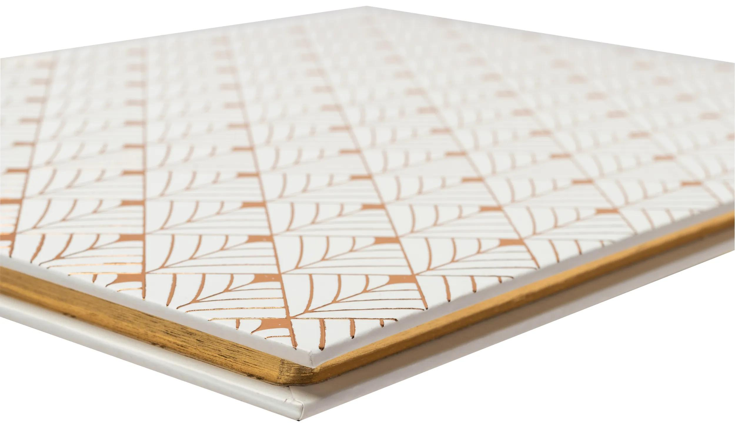 Un cuaderno blanco con un patrón de hojas doradas y bordes de página dorados.