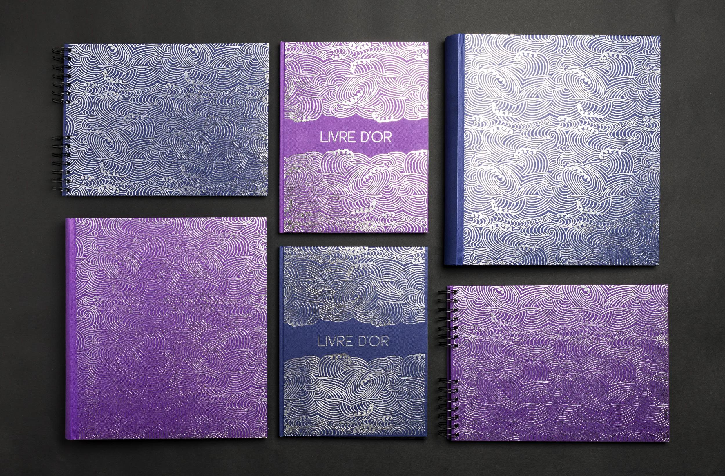 Seis cuadernos con patrón de olas plateadas sobre fondos azules y morados.