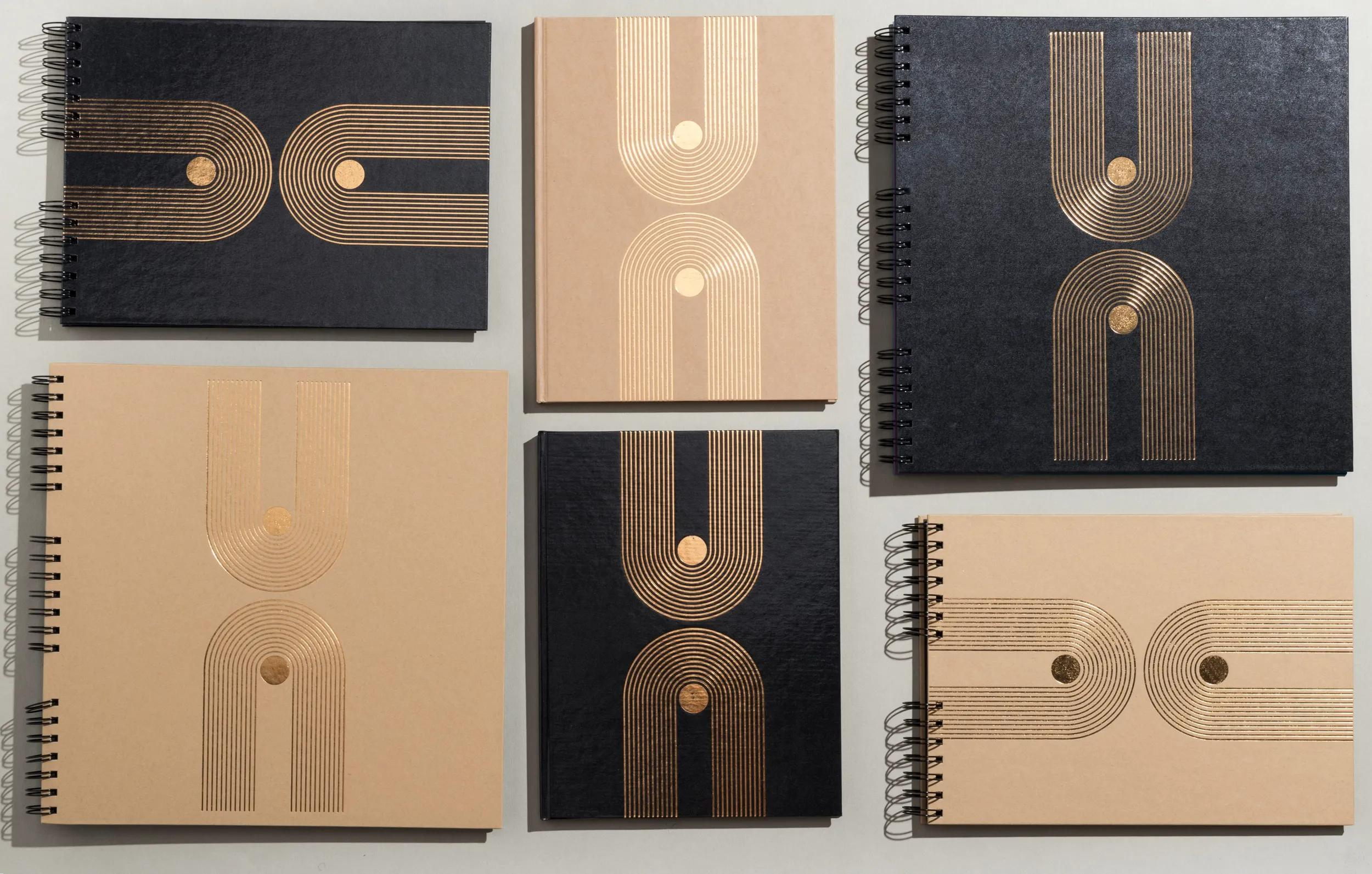 Seis cuadernos con diseños geométricos dorados sobre cubiertas negras y tostadas.
