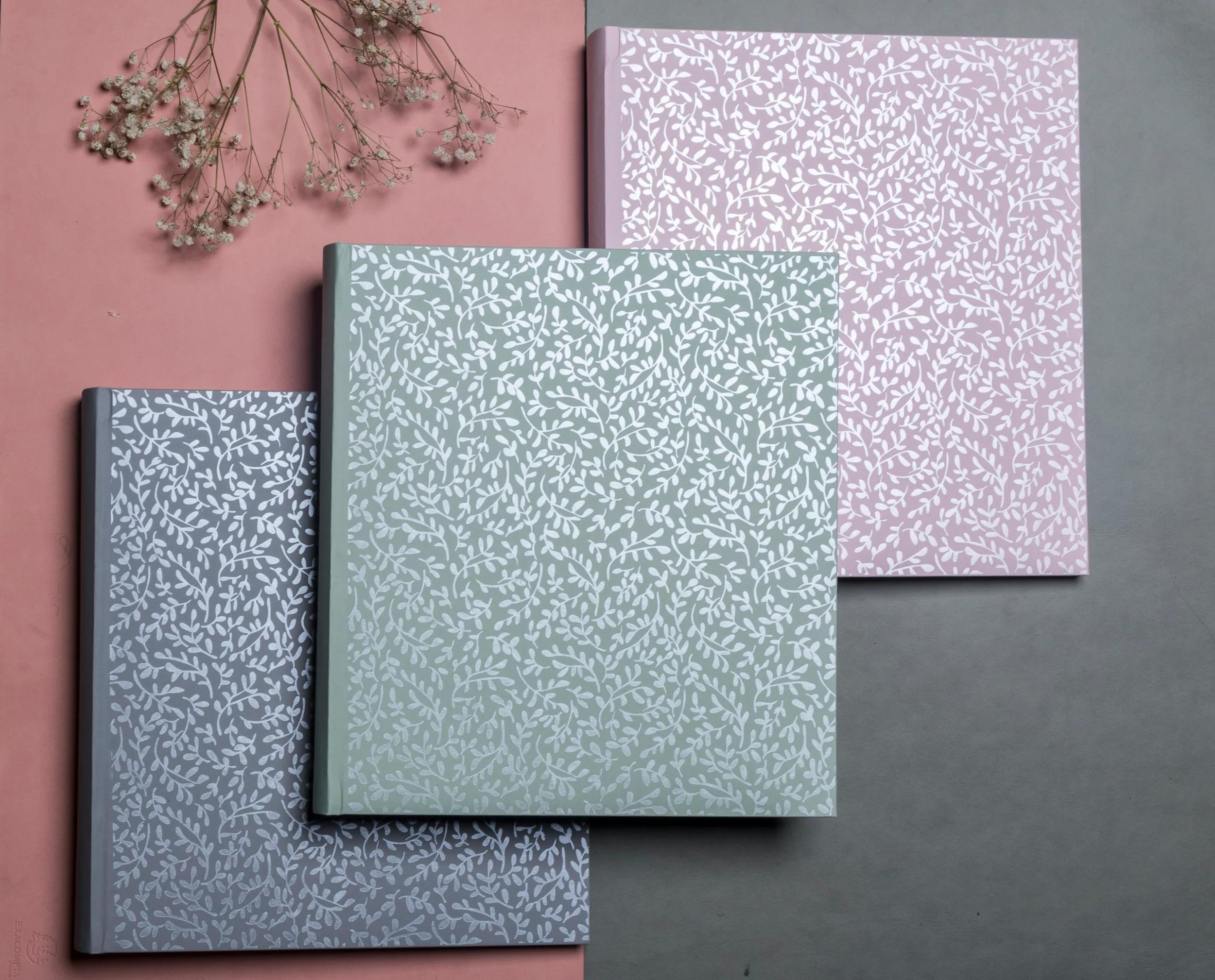 Tres cuadernos con estampado de hojas en gris, verde y rosa sobre fondo gris.