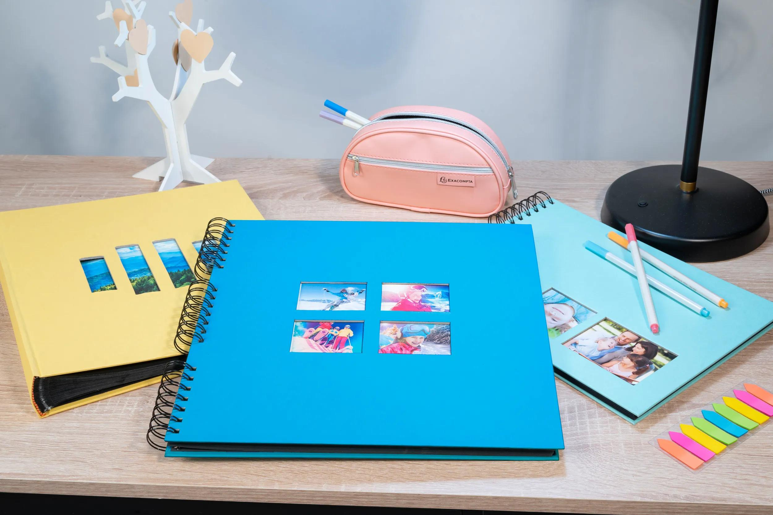 Un escritorio con tres álbumes de fotos, un estuche y la base de una lámpara.