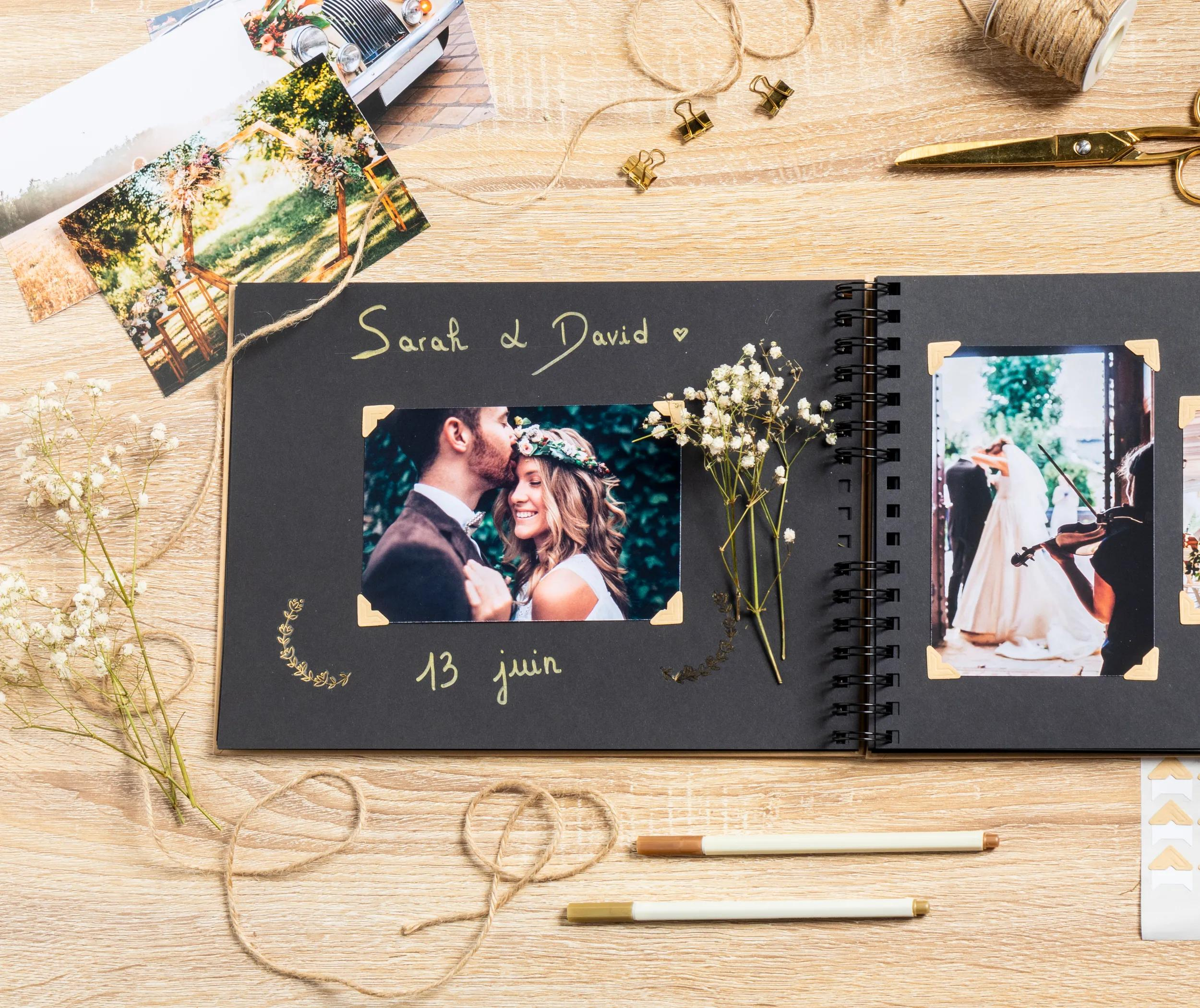 Álbum de bodas con fotos, flores y tijeras sobre mesa de madera.