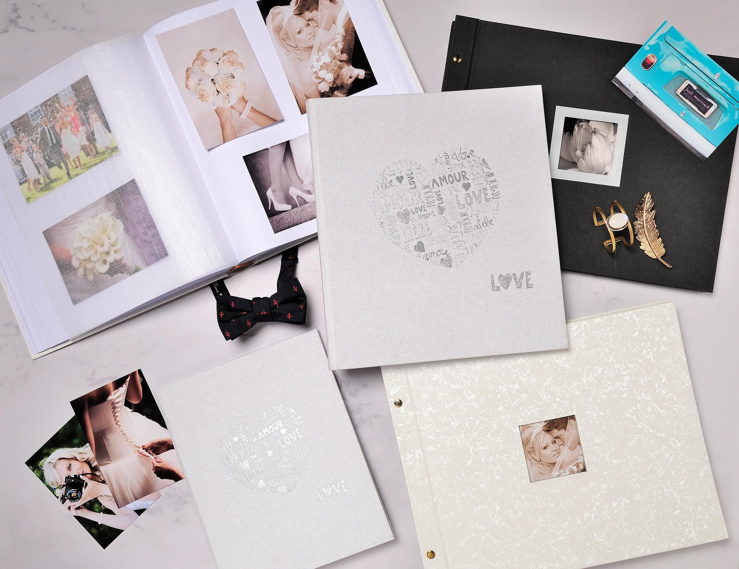 Álbumes de boda, fotos, pajarita y joyas sobre superficie de mármol.