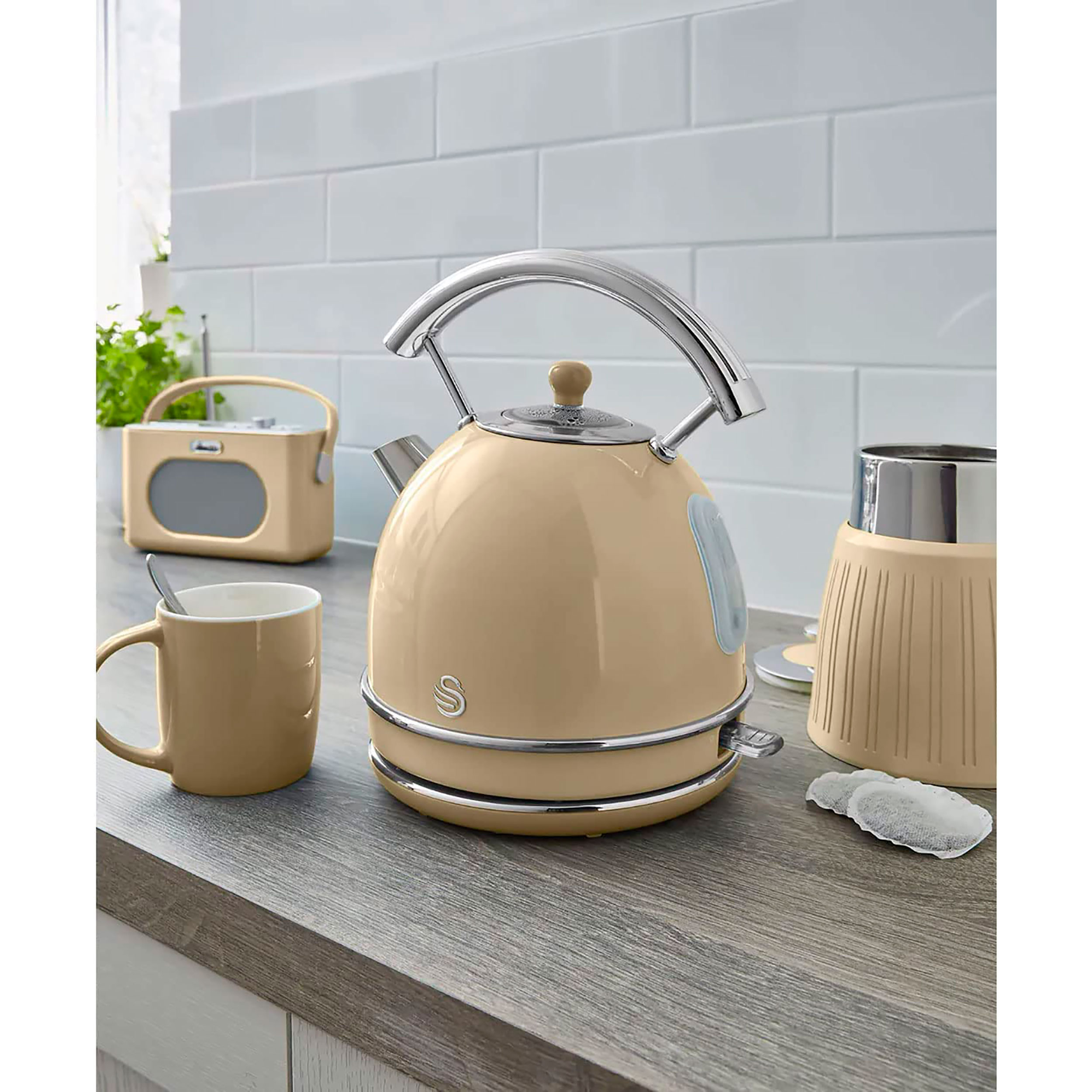 Eine beige Teekanne mit silbernem Griff und Tassenhalter auf einem Holztresen.