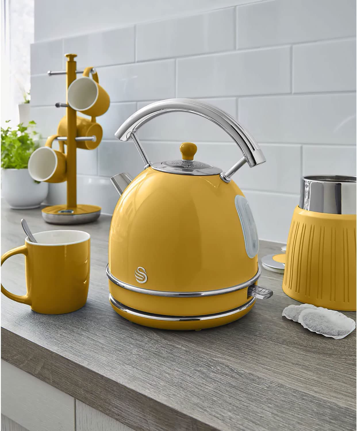 Eine gelbe Teekanne mit silbernem Griff steht auf einer Holzoberfläche neben einer Tasse.