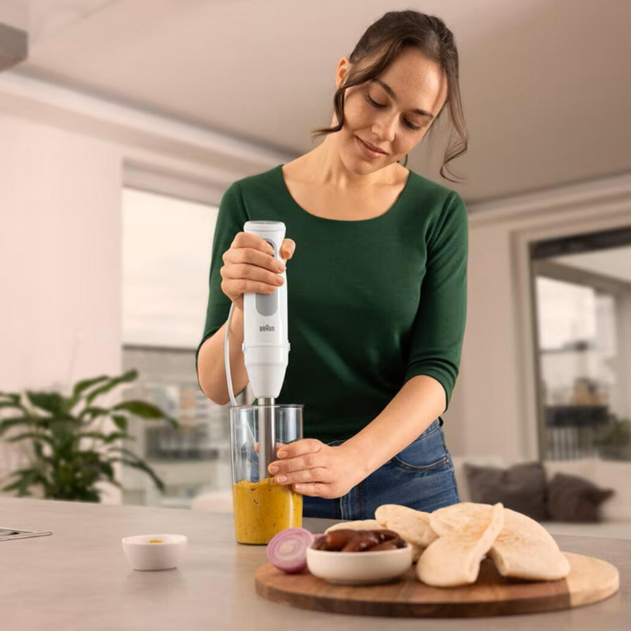 Een vrouw mixt een gele massa in een glas met een staafmixer.