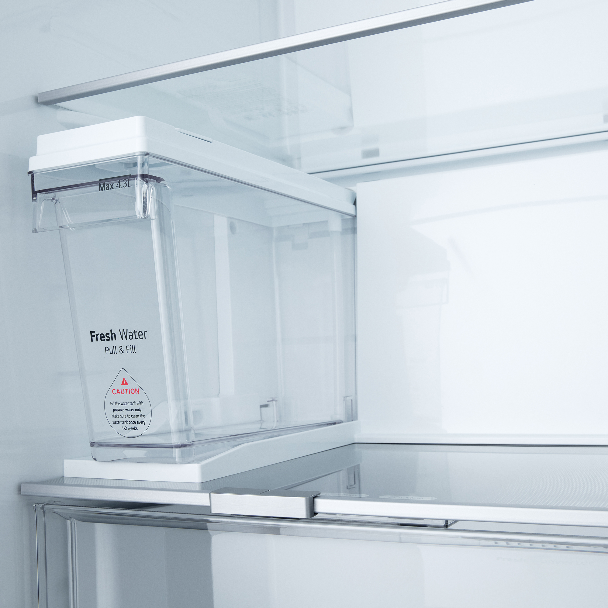 Ein transparenter Wassertank mit "Max 4,3L"-Markierung ist in einem Kühlschrankregal platziert.