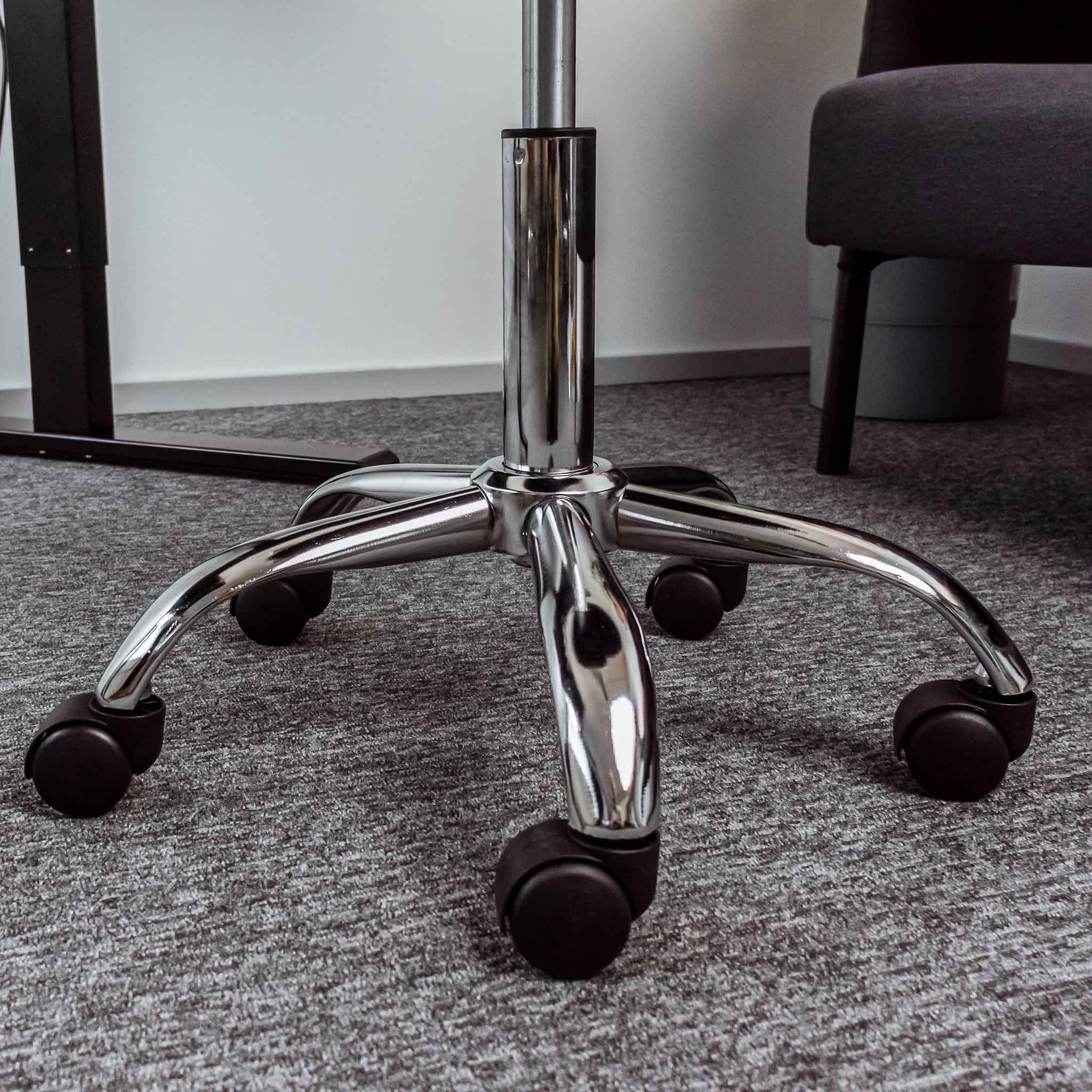 Chromowana podstawa krzesła biurowego z pięcioma kółkami na szarej wykładzinie.