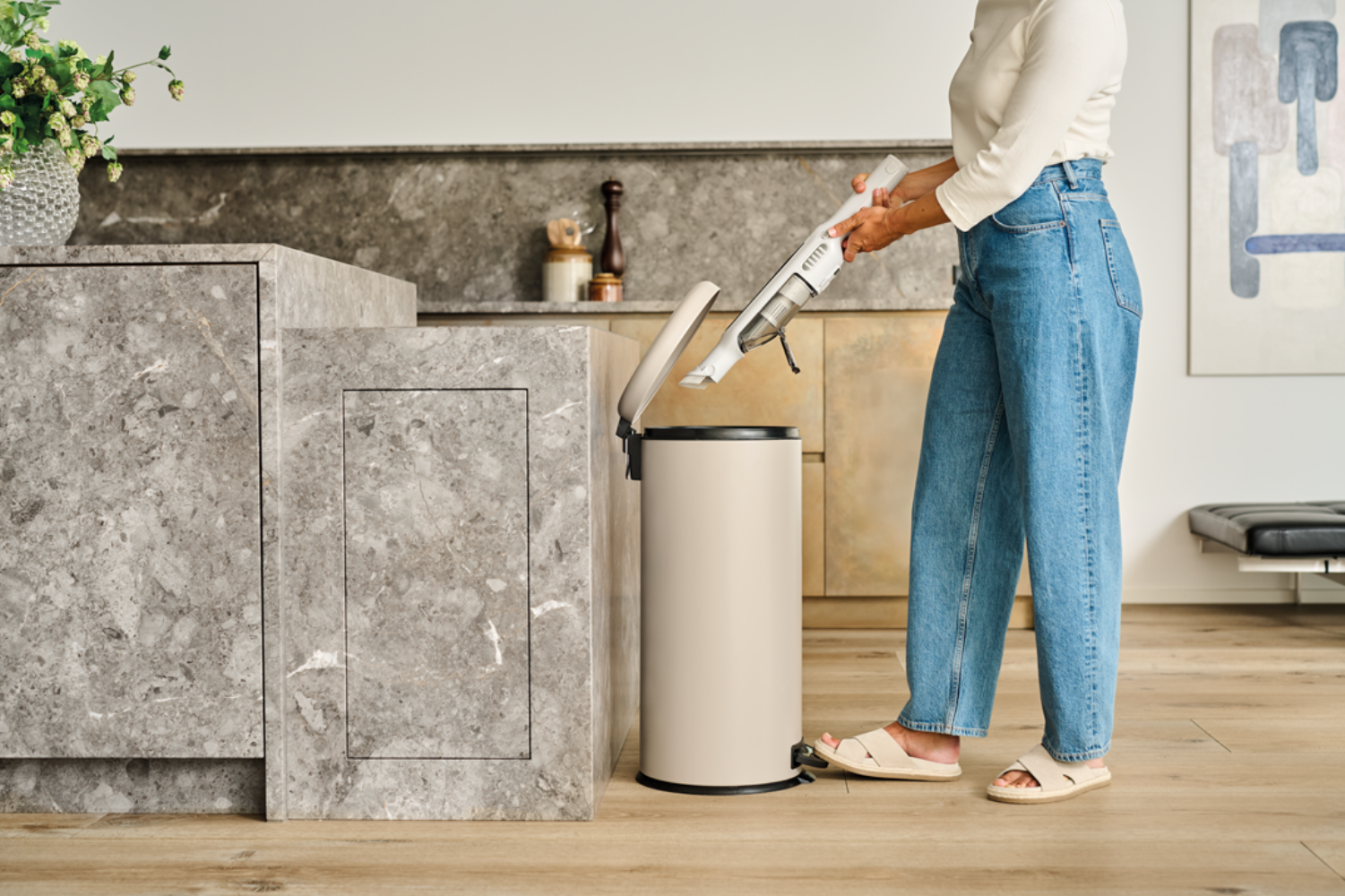 Une personne passe l'aspirateur dans une poubelle beige avec un aspirateur à main.
