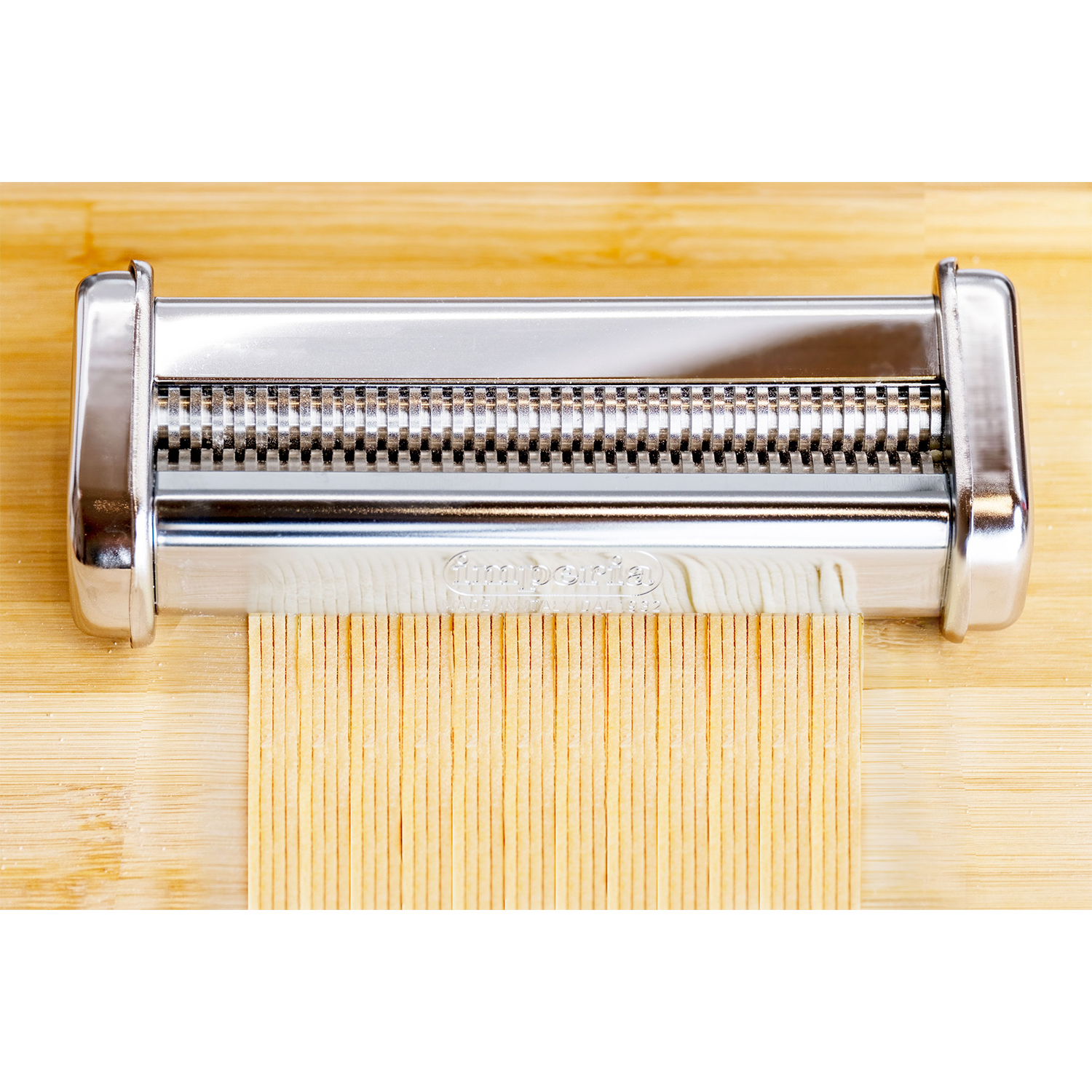 Una macchina per la pasta taglia l'impasto in spaghetti sottili su fondo di legno.