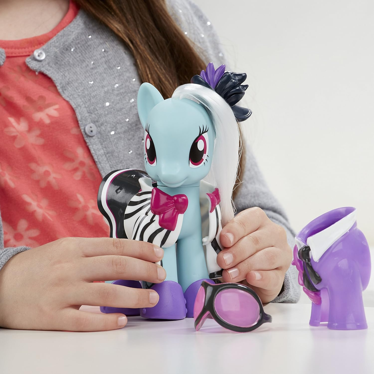 Ein blaues Pony-Spielzeug mit Zebra-Akzenten, Brille und lila Figur.