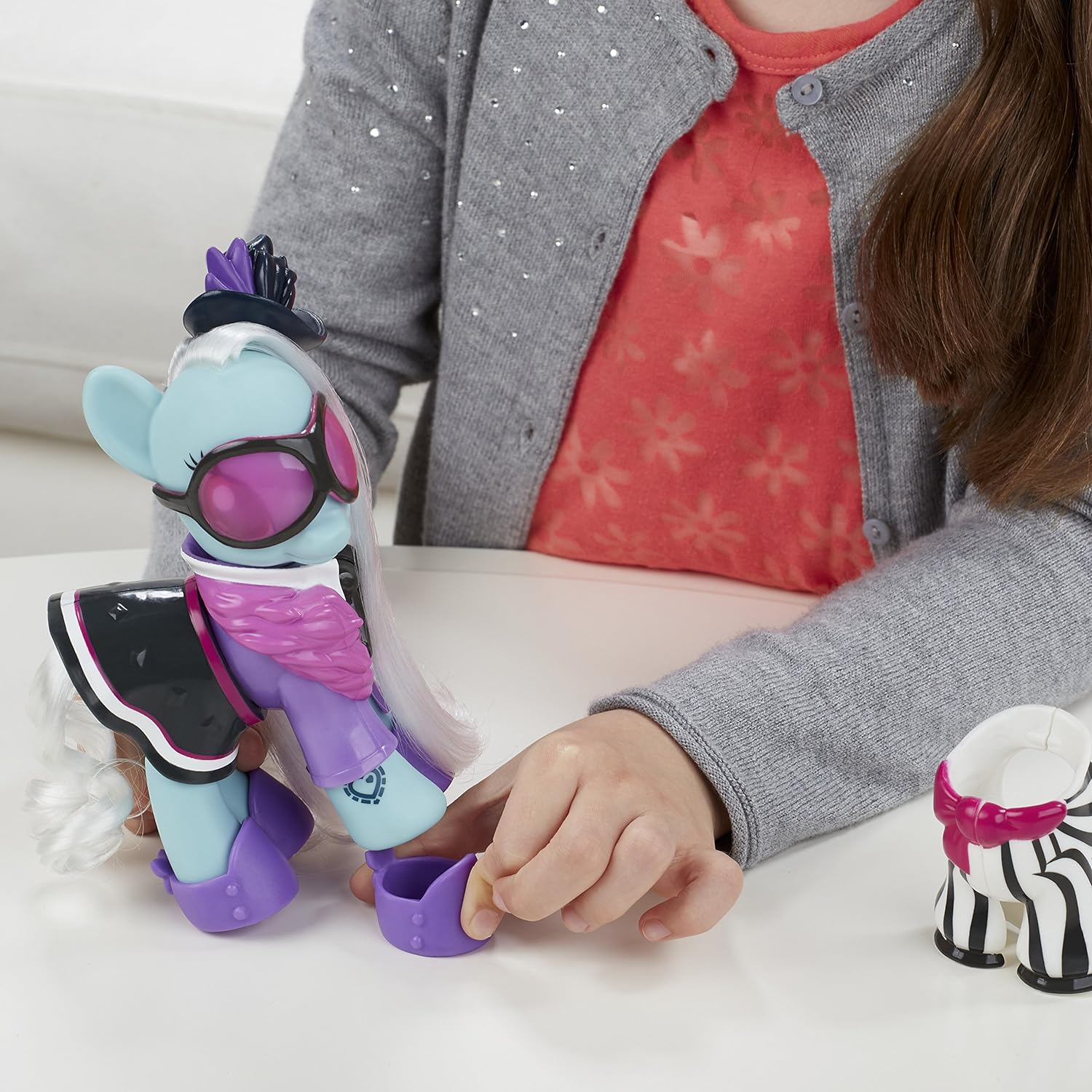 Ein blaues Pony-Spielzeug mit Hut und Brille, daneben ein Zebra-Accessoire.