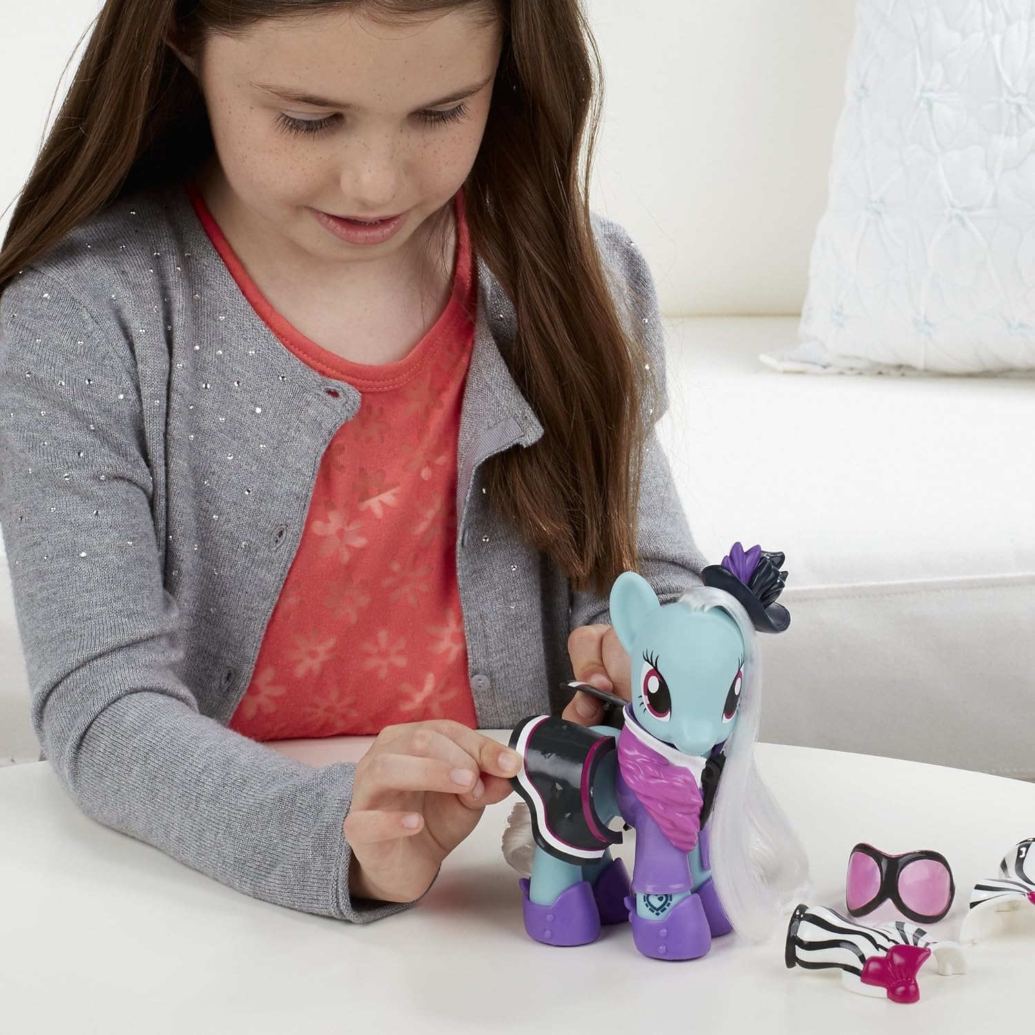 Mädchen spielt mit blauem Pony-Spielzeug und Zubehör auf einem Tisch.