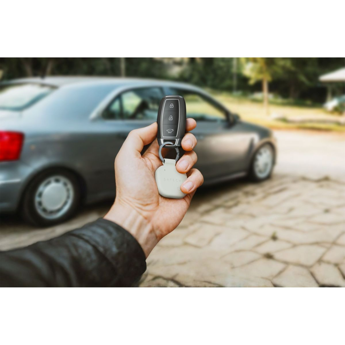 Eine Hand hält einen Autoschlüssel mit Anhänger vor einem grauen Auto.