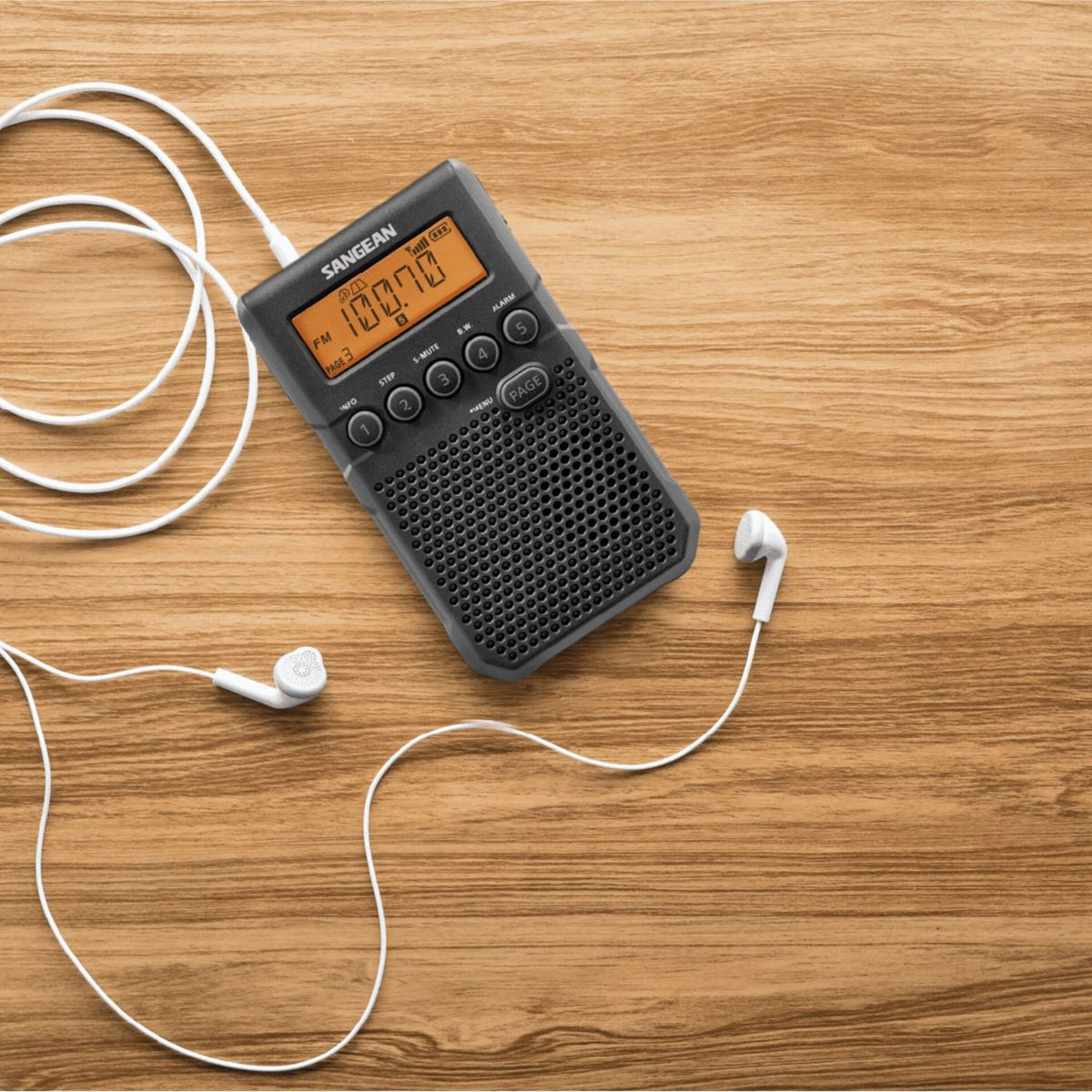 Una radio Sangean nera con auricolari bianchi su legno. Mostra 100.70 FM.