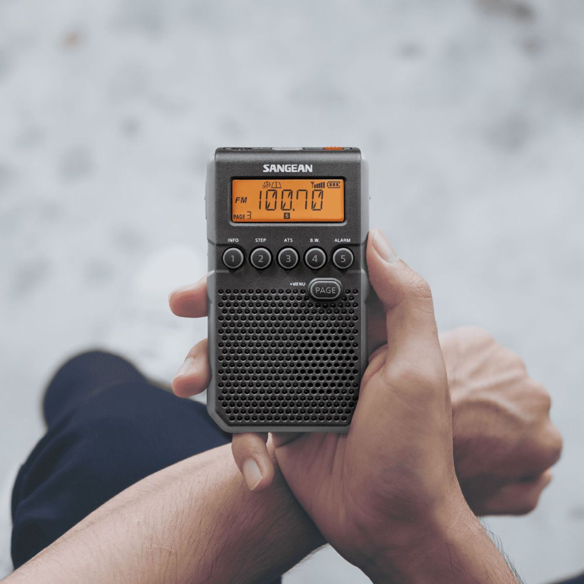 Una mano tiene una piccola radio Sangean nera con display arancione.