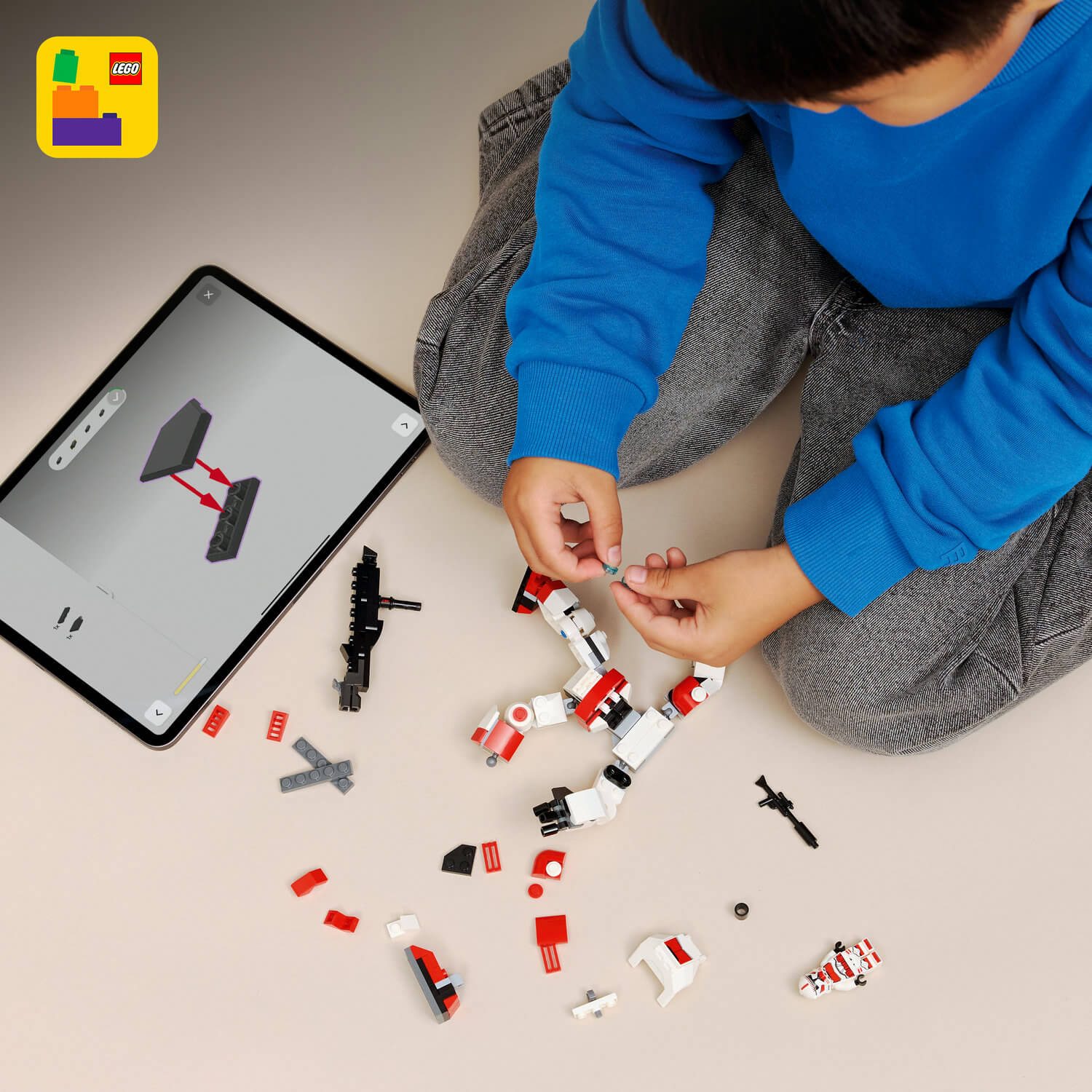 Çocuk, tablet üzerindeki talimatları izleyerek kırmızı ve beyaz Lego tuğlalarıyla inşa ediyor.
