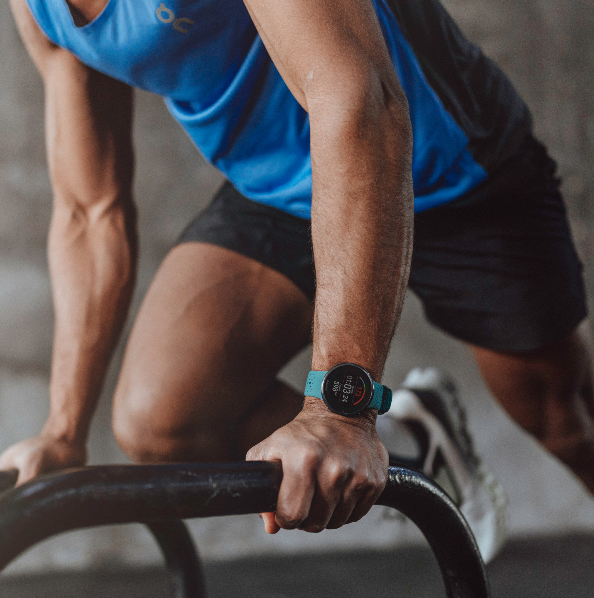 Mężczyzna w niebieskiej koszulce bez rękawów i czarnych spodenkach robi pompki, nosi turkusowy zegarek.